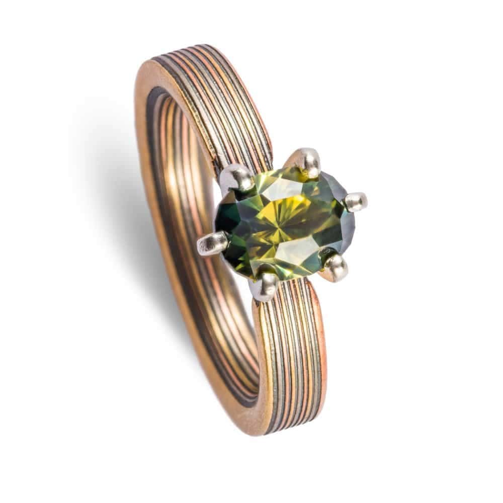 beautiful engagement style mokume gane ring, linear straight across pattern, with a pretty green sapphire in prongs