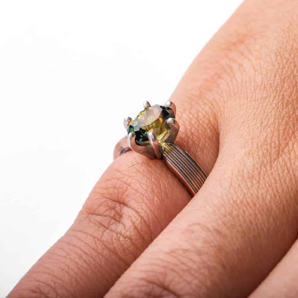 beautiful engagement style mokume gane ring, linear straight across pattern, with a pretty green sapphire in prongs