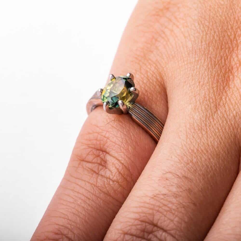beautiful engagement style mokume gane ring, linear straight across pattern, with a pretty green sapphire in prongs