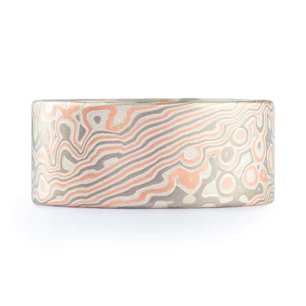 Wide ring with a flat profile, made with red gold, palladium (gray) and silver (light gray), in a twisting and speckled style pattern. Â