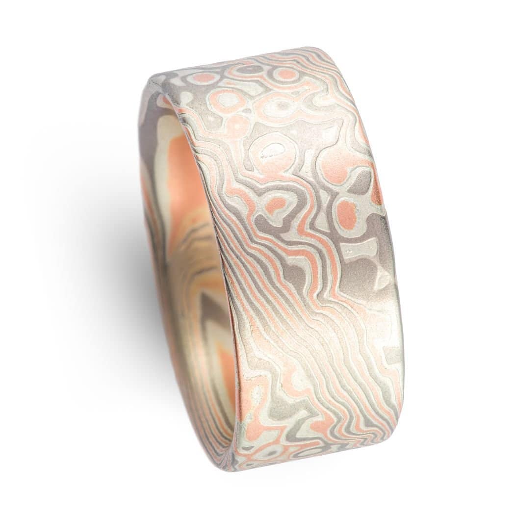 Wide ring with a flat profile, made with red gold, palladium (gray) and silver (light gray), in a twisting and speckled style pattern. Â