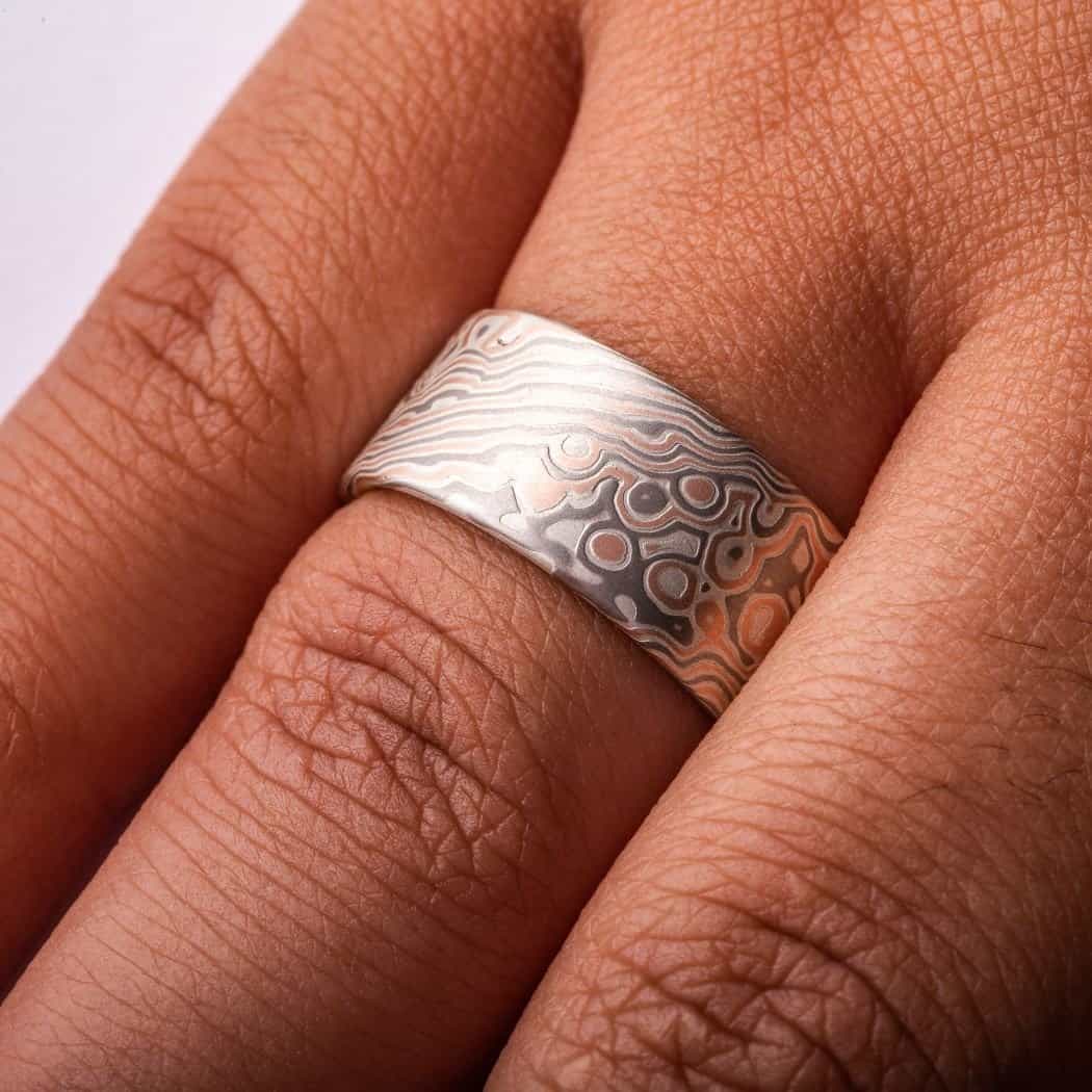 Wide ring with a flat profile, made with red gold, palladium (gray) and silver (light gray), in a twisting and speckled style pattern. Â