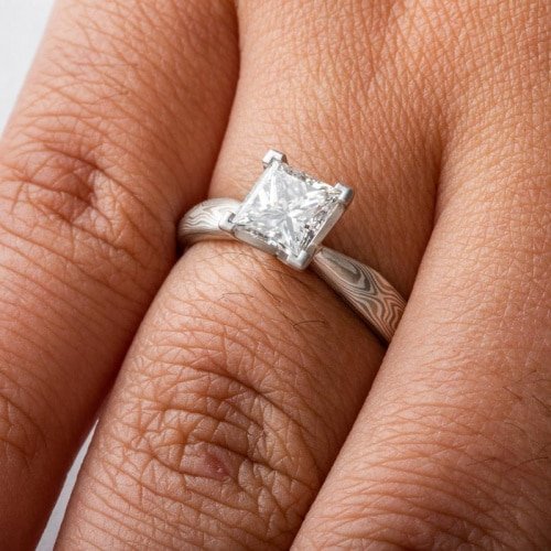 solitaire style mokume gane engagement ring with square diamond set in prongs, ring has an overall silvery palette and a woodgrain style pattern