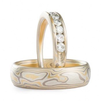 This elegant set of Mokume Gane rings, featuring a 4mm and 6mm width, is shown in the Woodgrain pattern and the Flare metal combination. Both rings have a low dome profile and an etched finish. The Flare palette includes 14k yellow gold, silver, and palladium. The narrower ring is gently tapered and showcases 5 beautiful channel-set moissanites.