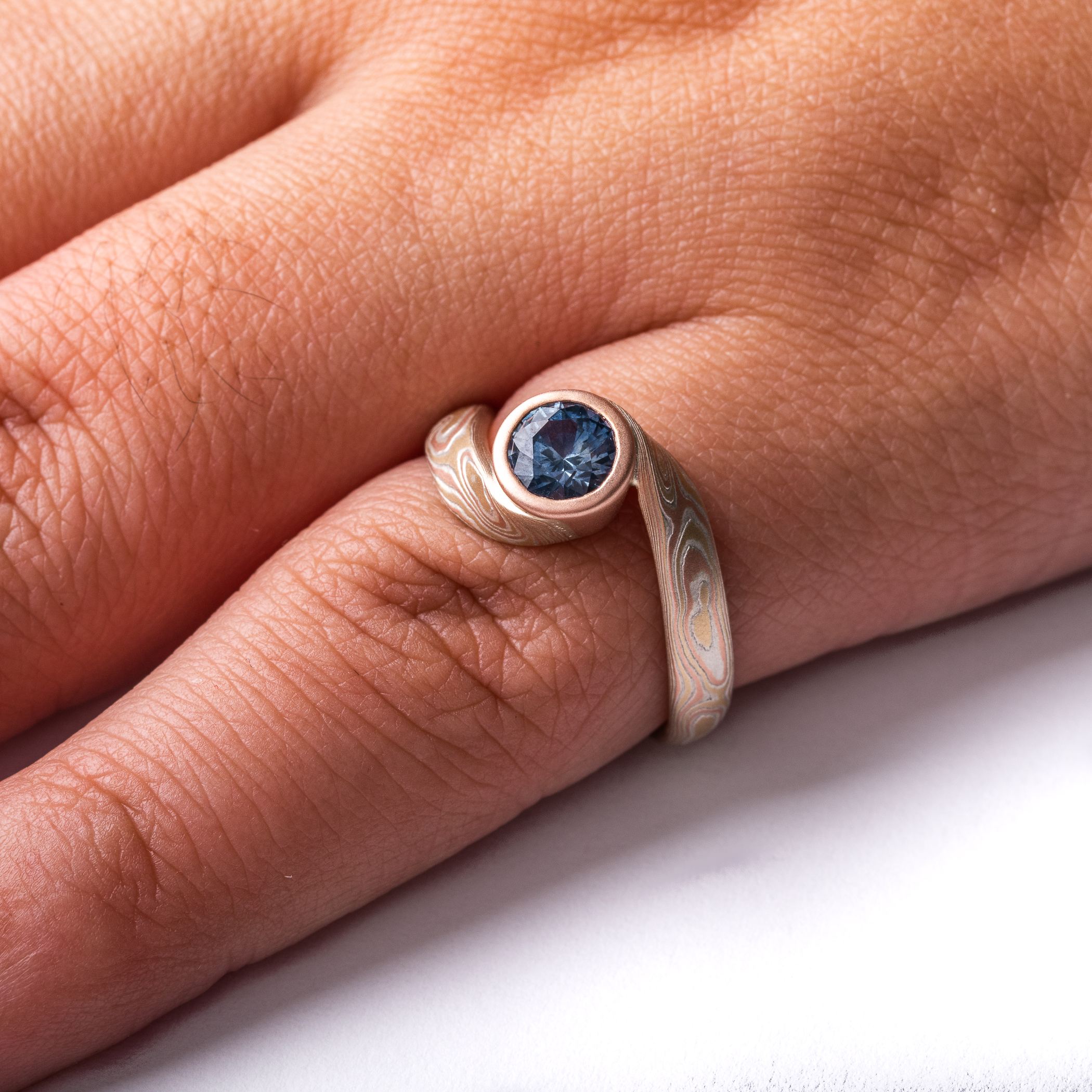 deep blue sapphire circled with red gold and yellow gold and silver in woodgrain patterned ring