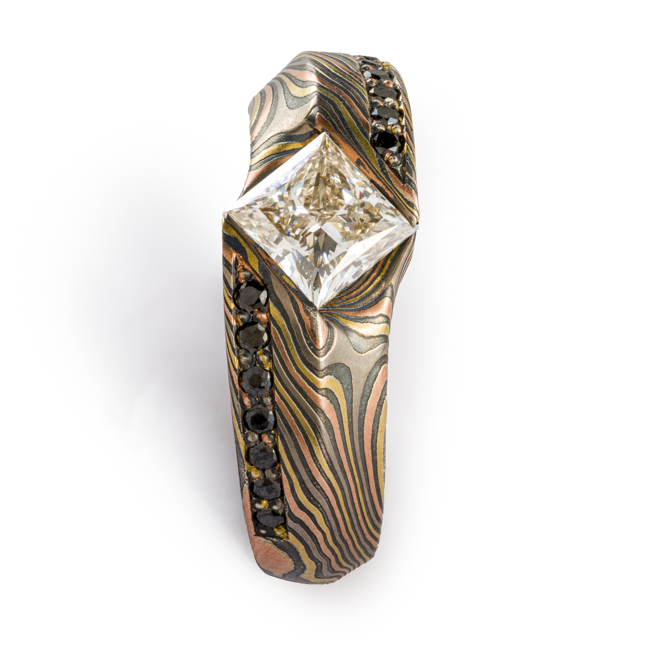 This is a custom made Mokume Gane ring, made by arn krebs, featuring a unique carved angled profile and a modified cathedral style setting holding the large white center diamond. The diamond is square and set diagonally to the band, and is flanked on each side by seven small bead set black diamonds running parallel to the band. It's made in our Twist pattern and an upgraded 18kt version of our Firestorm palette, the metals in it are red gold yellow gold palladium and silver
