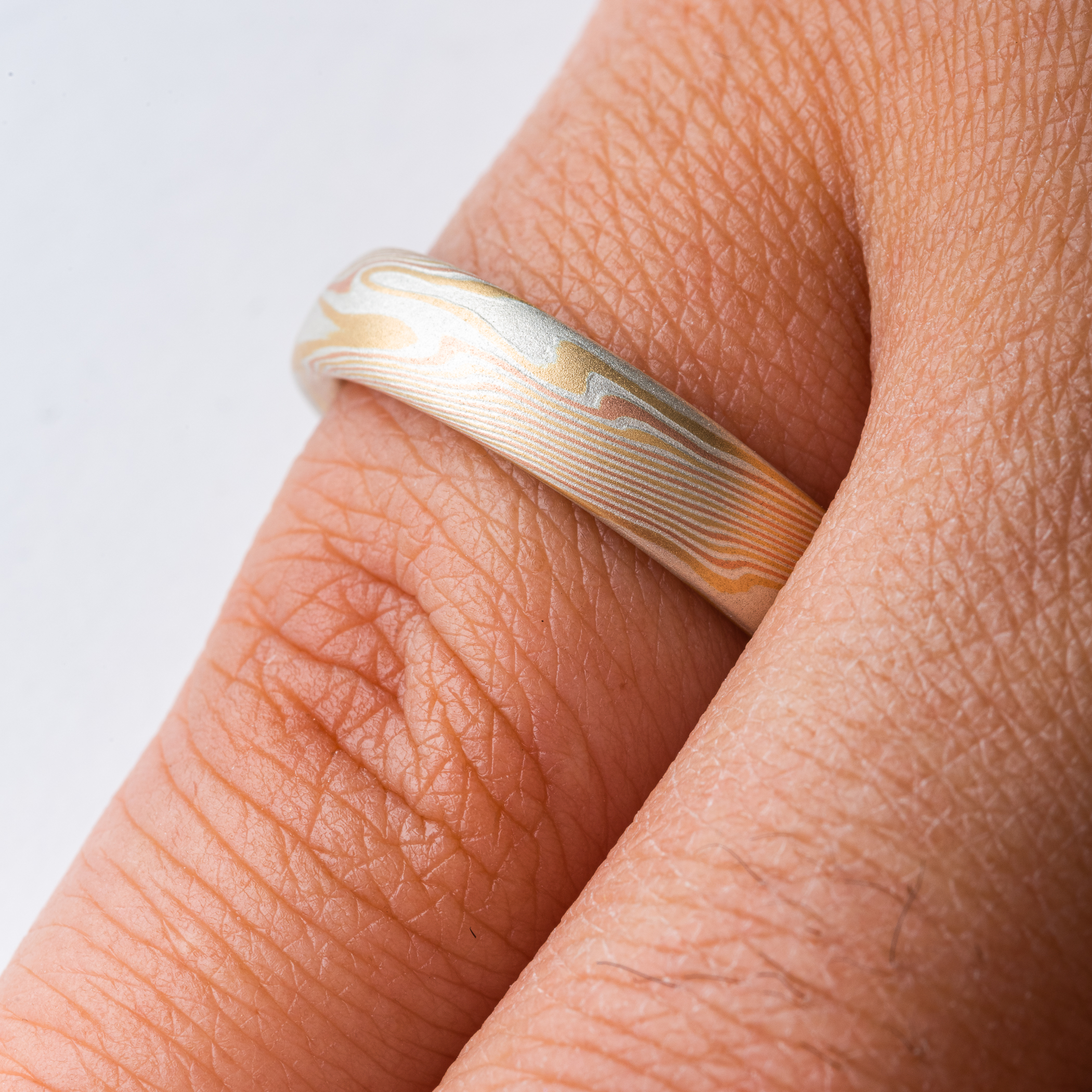 Yellow and red gold mokume gane patterned ring, made in an organic twisting pattern that resembles wood grain.