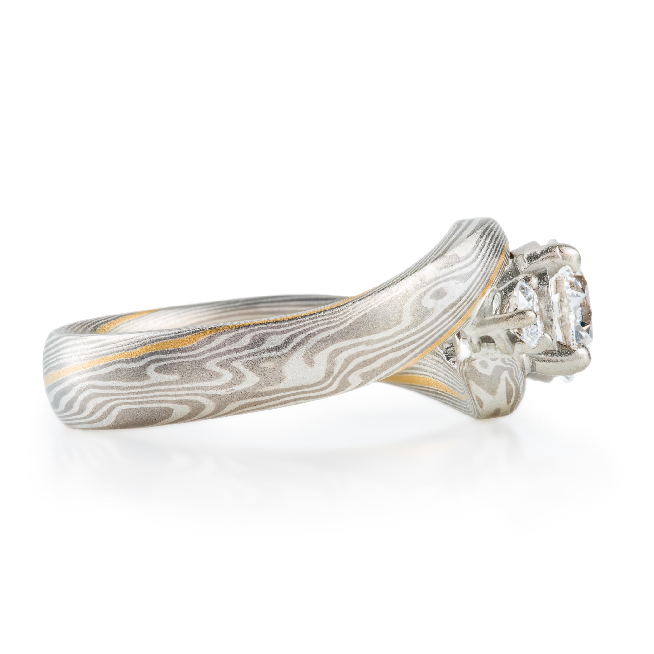 mokume gane wedding ring, band is twisted around the setting in the center, three diamonds, a larger one in the center with two smaller side stones.