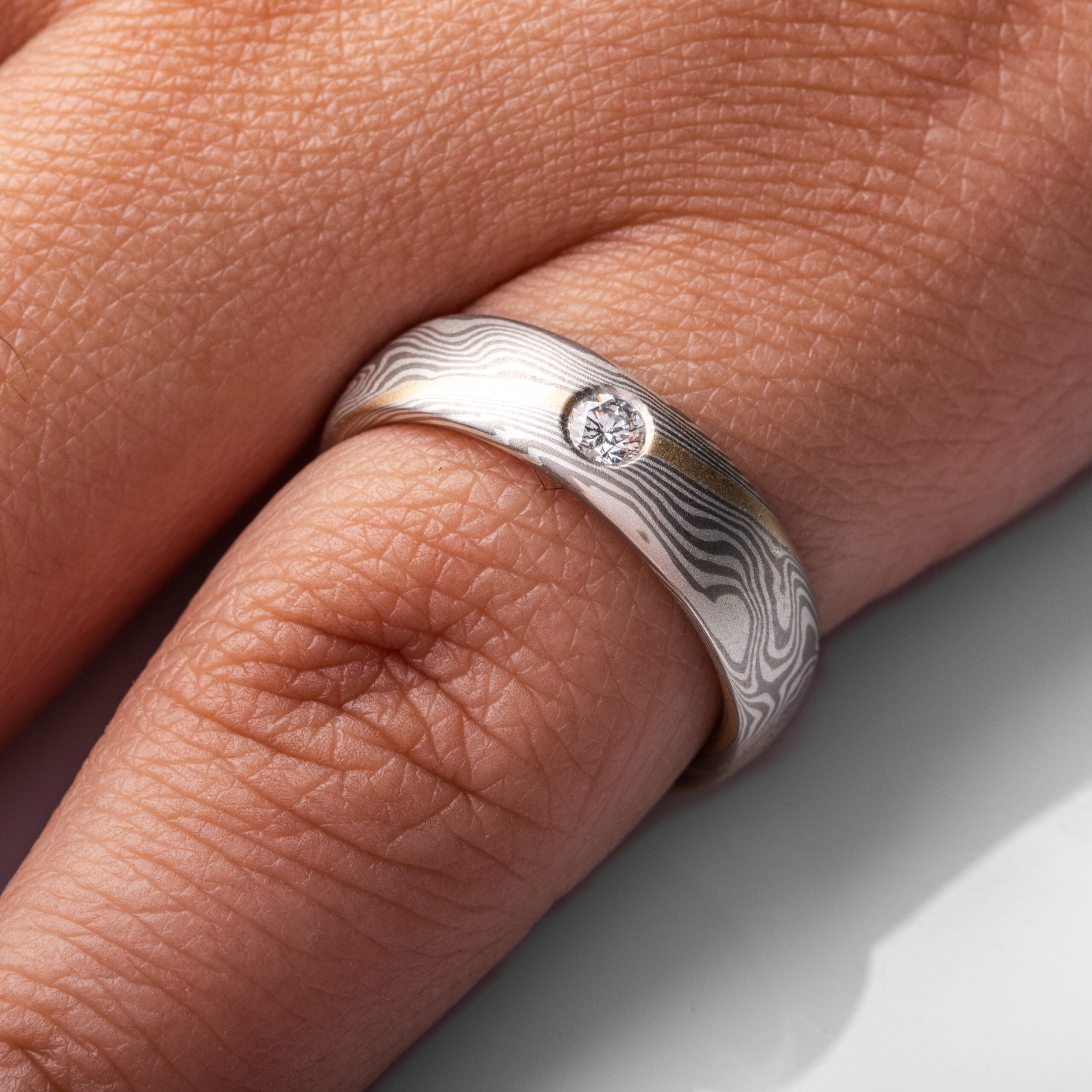 mokume gane band with a flush set diamond and an added yellow gold stratum layer