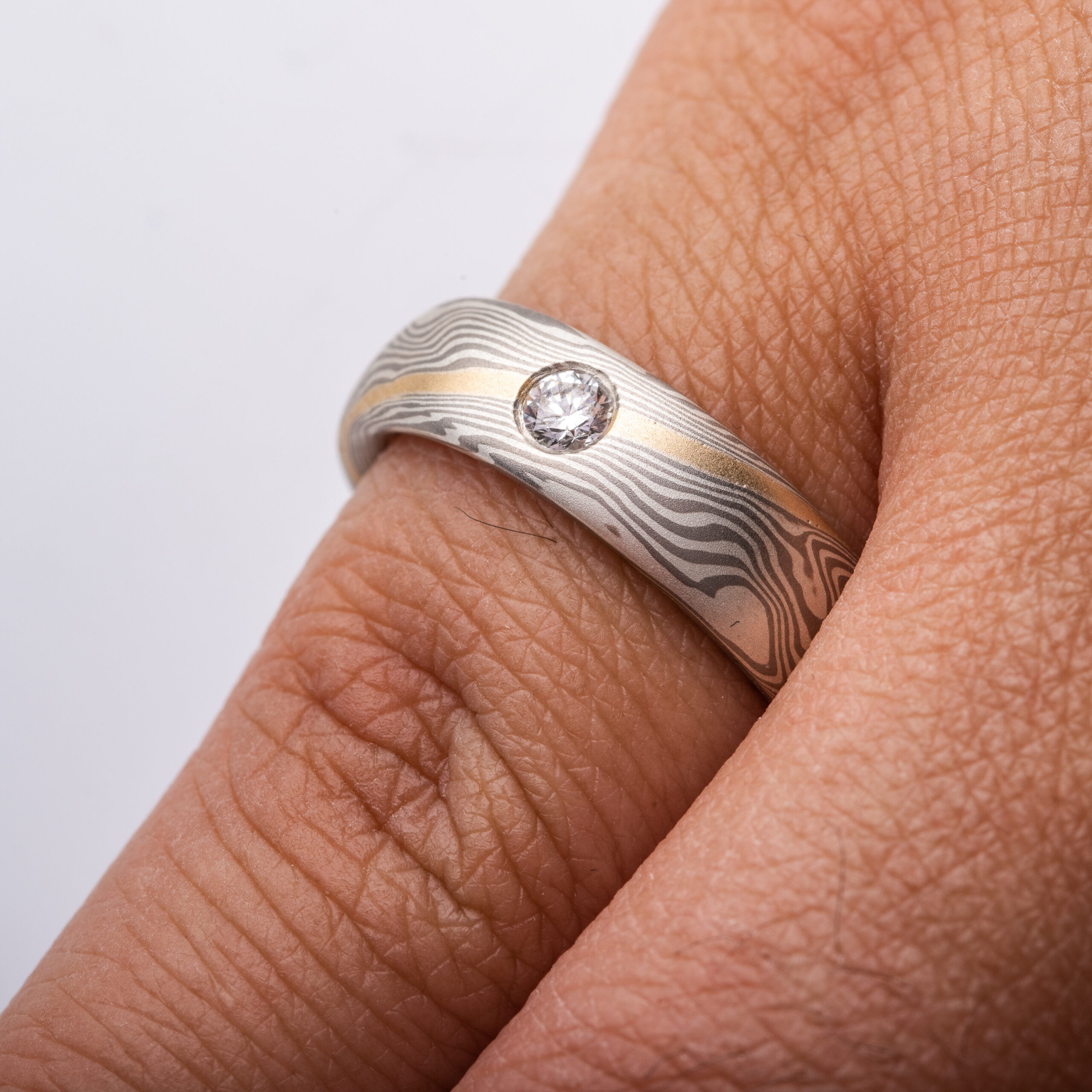 mokume gane band with a flush set diamond and an added yellow gold stratum layer