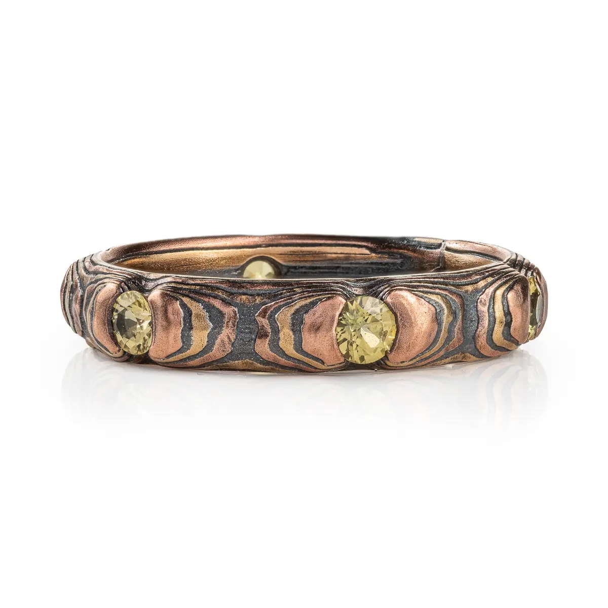 Small and dainty mokume gane ring patterned in a textured style with red and yellow gold, and with small yellow stones.