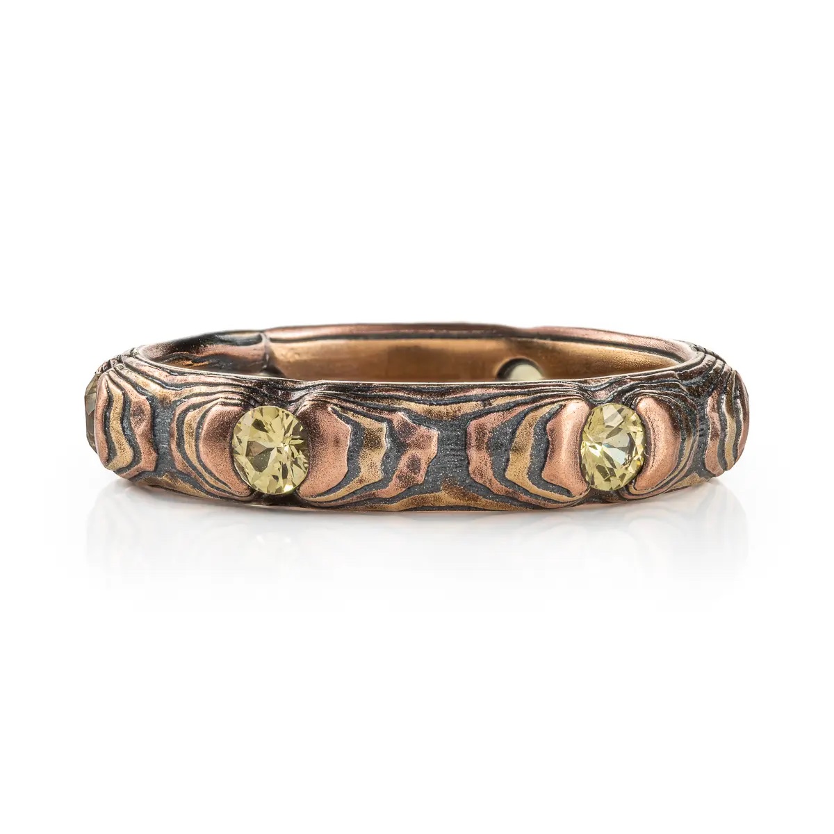 Small and dainty mokume gane ring patterned in a textured style with red and yellow gold, and with small yellow stones.
