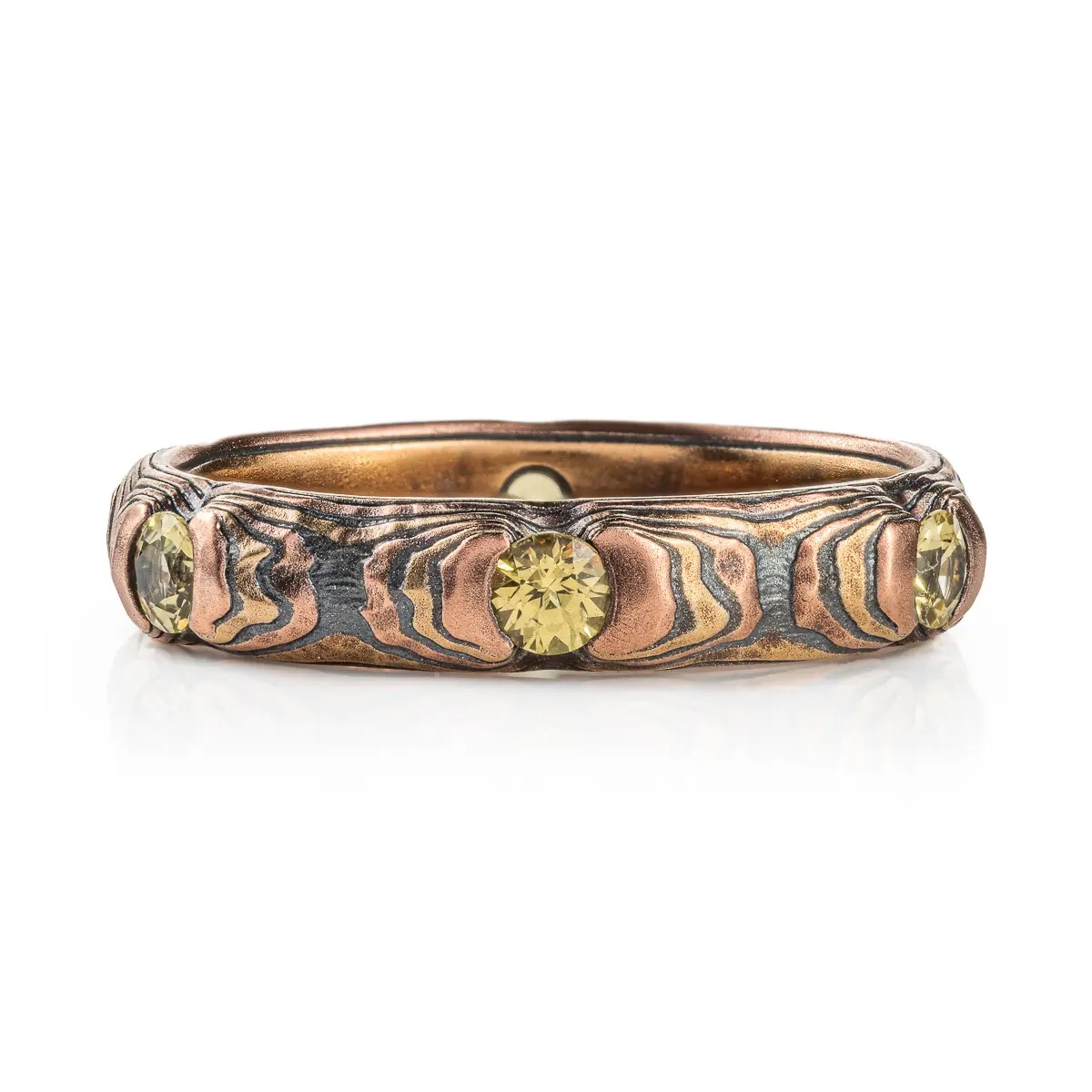 Small and dainty mokume gane ring patterned in a textured style with red and yellow gold, and with small yellow stones.