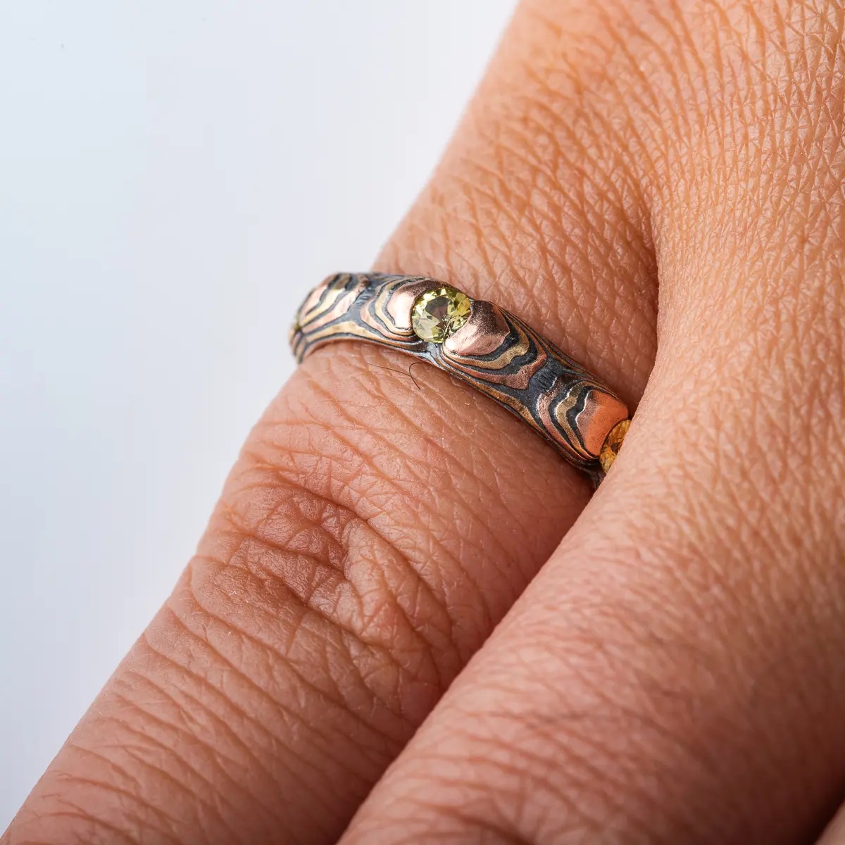 Small and dainty mokume gane ring patterned in a textured style with red and yellow gold, and with small yellow stones.