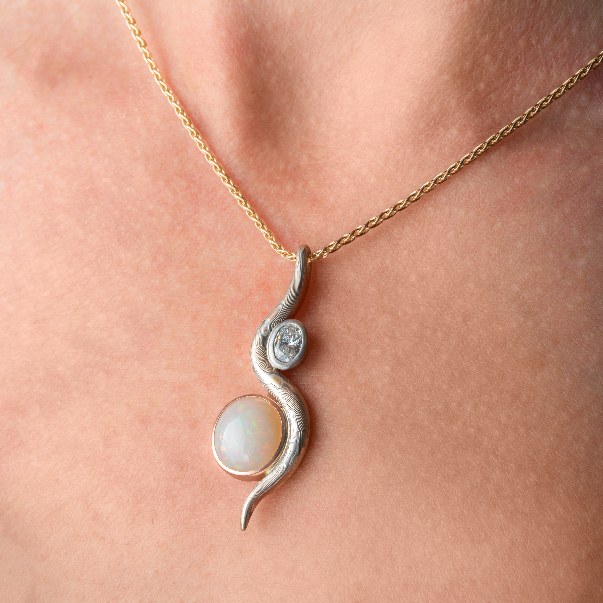 Elegant pendant made with a slender snake of patterned mokume gane gently curling around two oval shaped stones.