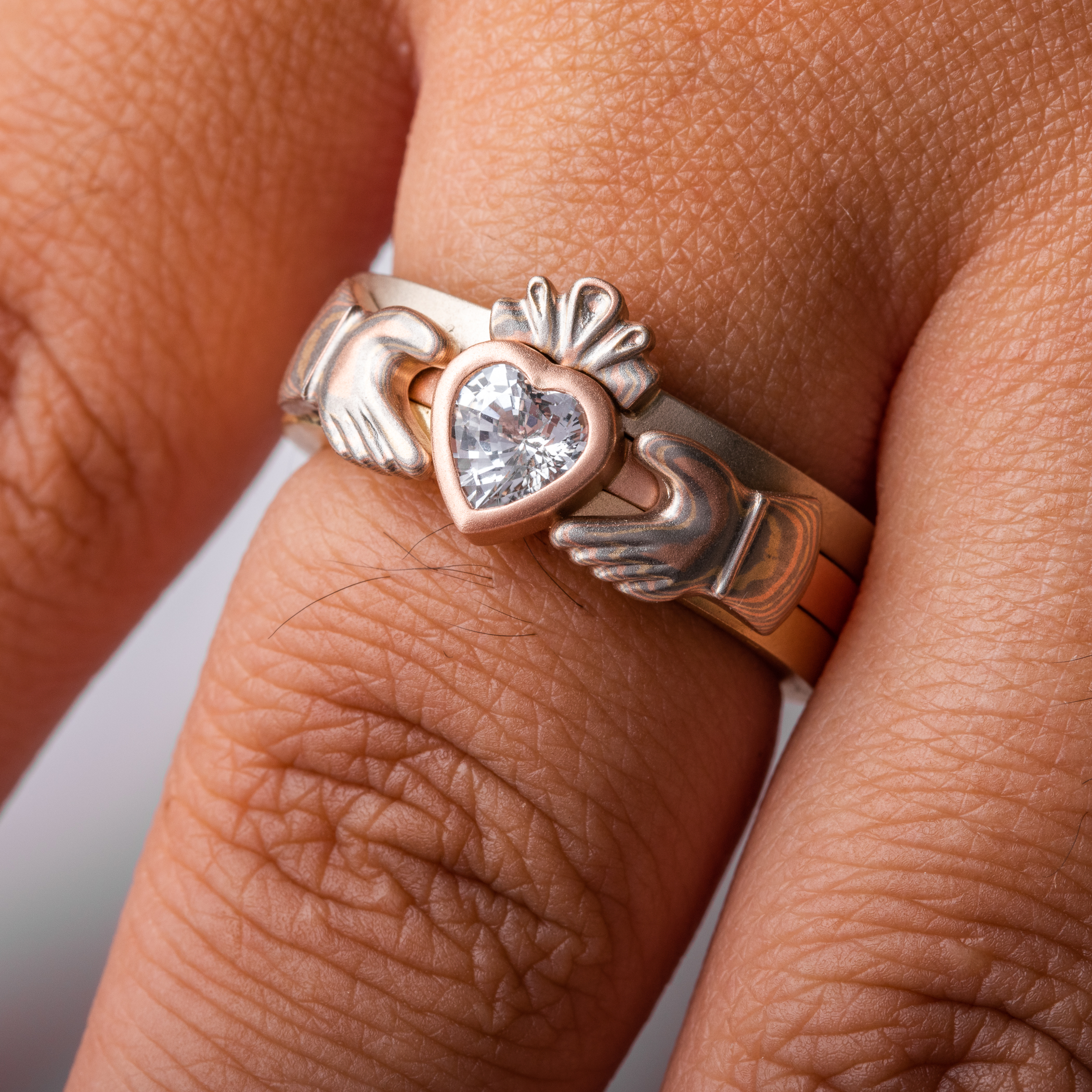 custom made three part claddagh ring, with mokume hands holding a white sapphire heart shaped stone, with a mokume crown on top of the stone
