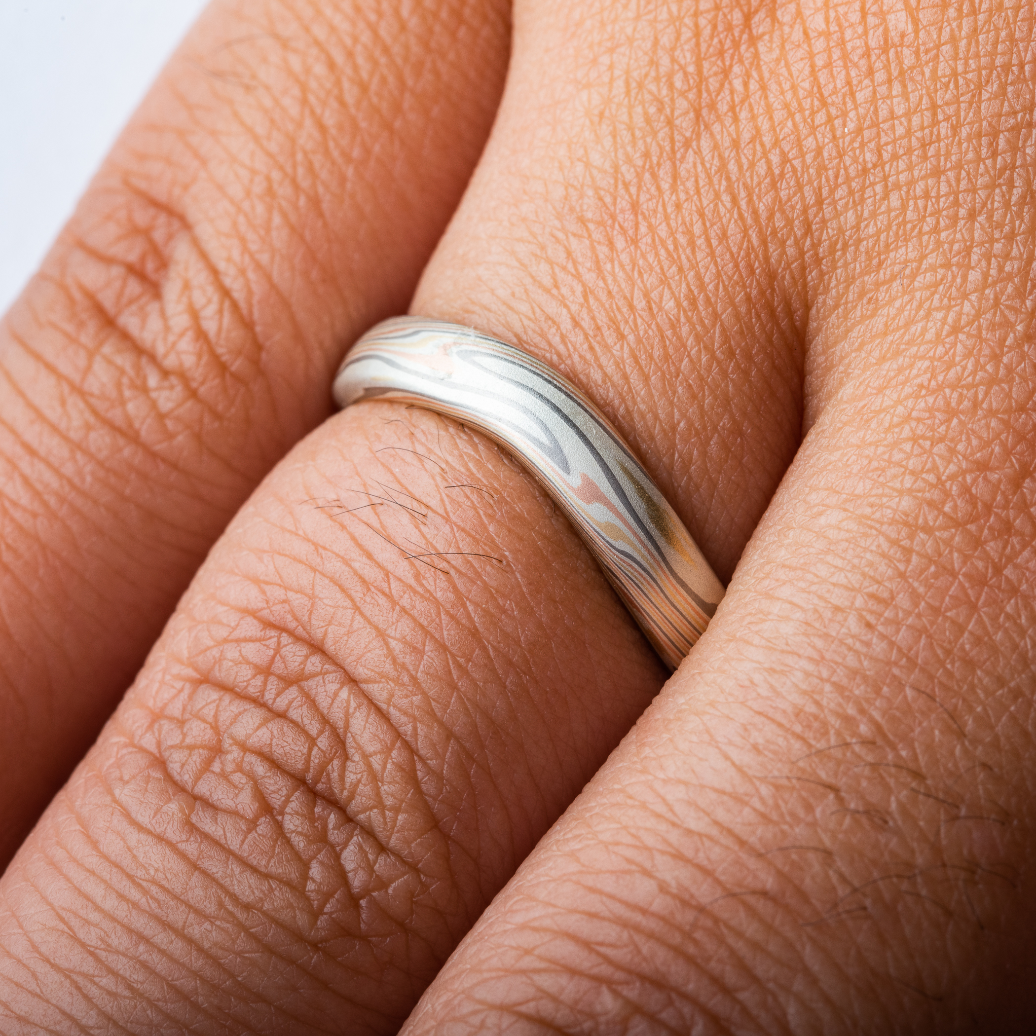 Gently curved mokume gane patterned band made to fit perfectly around an engagement ring. Made with red gold, yellow gold, palladium and silver.
