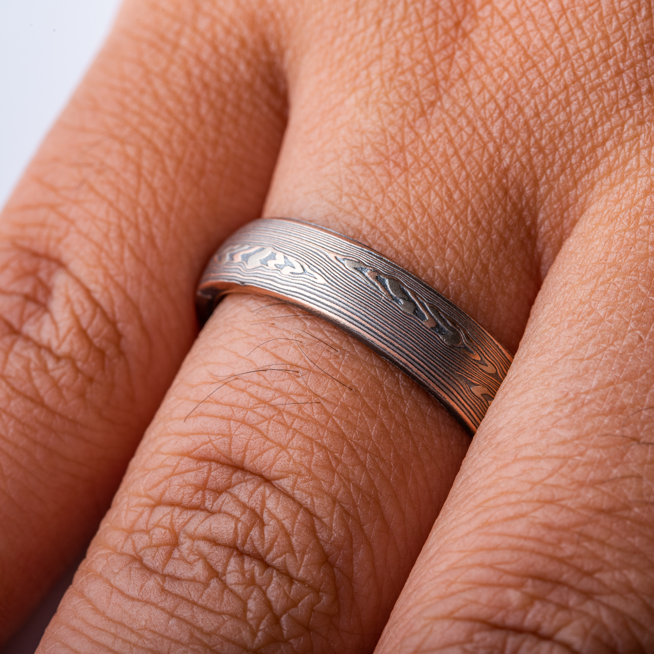 mokume patterned ring made with mainly linear pattern running parallel around the ring, with some areas of increased details, overall darker reddish tone