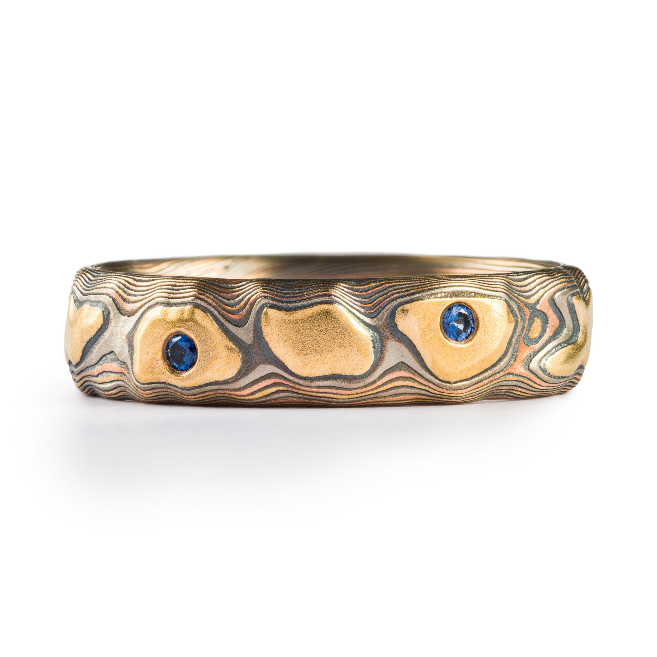 Mokume gane textured ring featuring yellow gold with snall round blue stones set flush into the band.