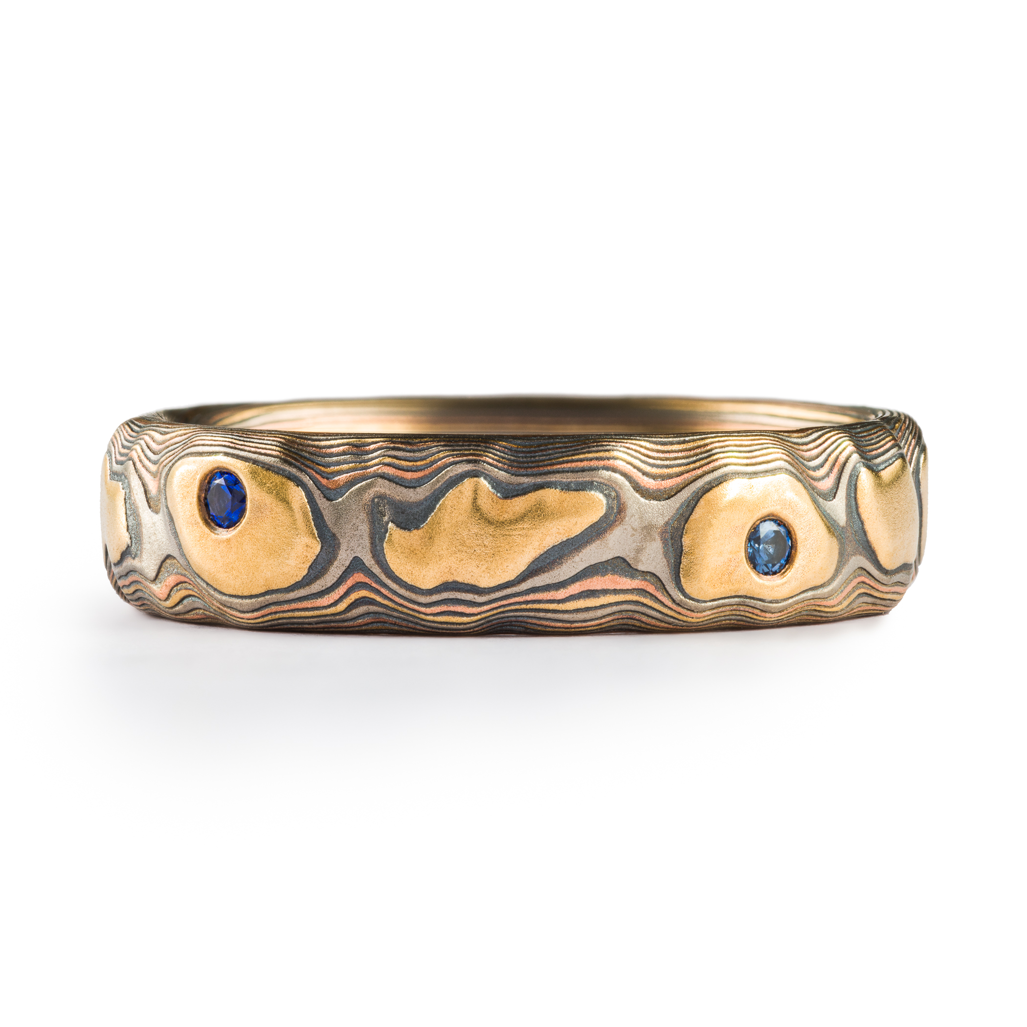 Mokume gane textured ring featuring yellow gold with snall round blue stones set flush into the band.