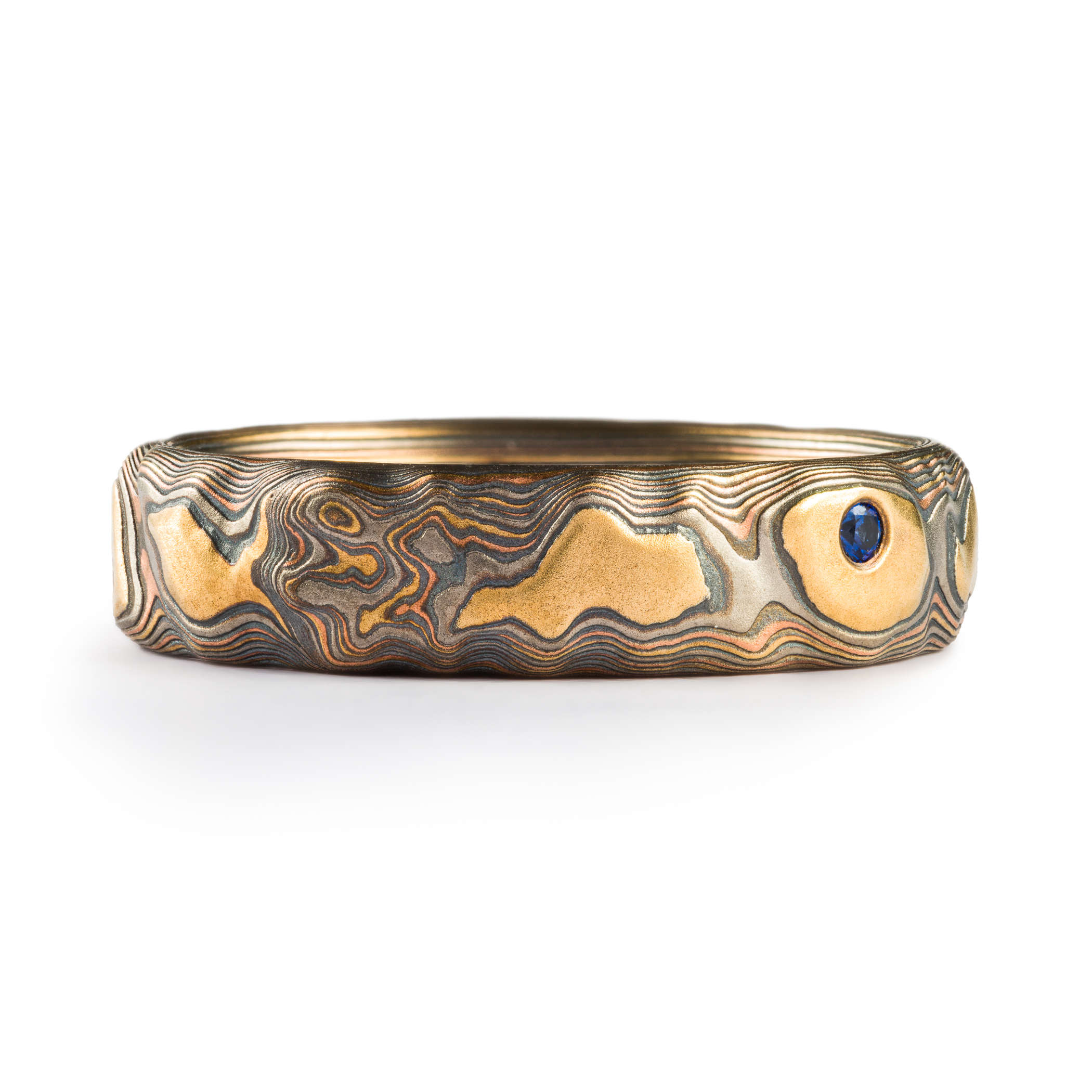 Mokume gane textured ring featuring yellow gold with snall round blue stones set flush into the band.