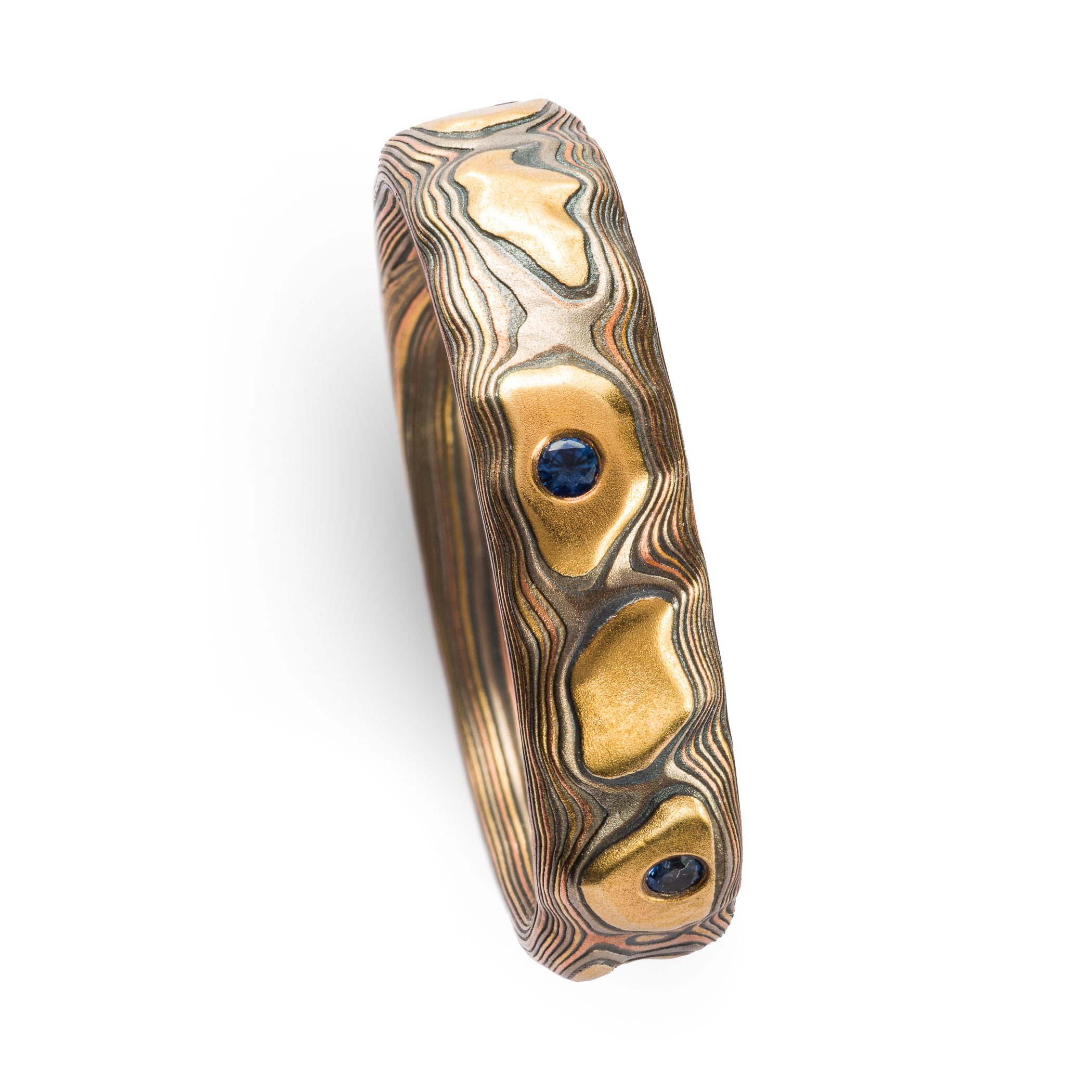 Mokume gane textured ring featuring yellow gold with snall round blue stones set flush into the band.