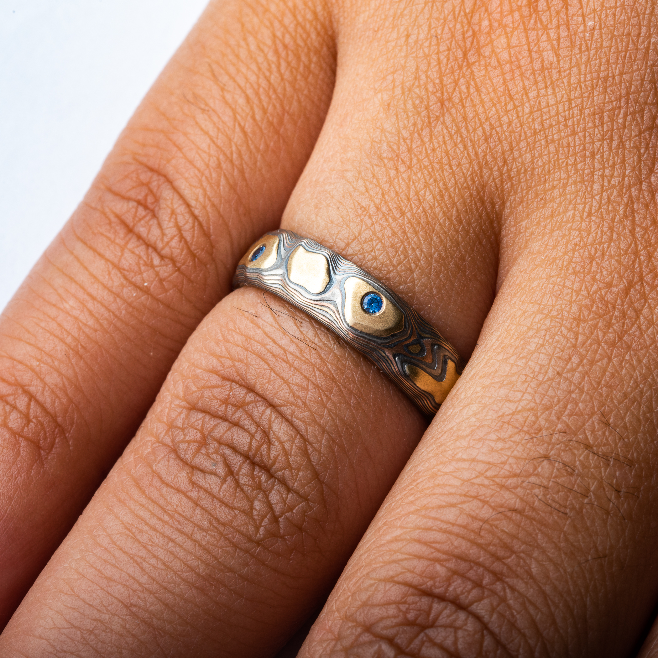 Mokume gane textured ring featuring yellow gold with snall round blue stones set flush into the band.