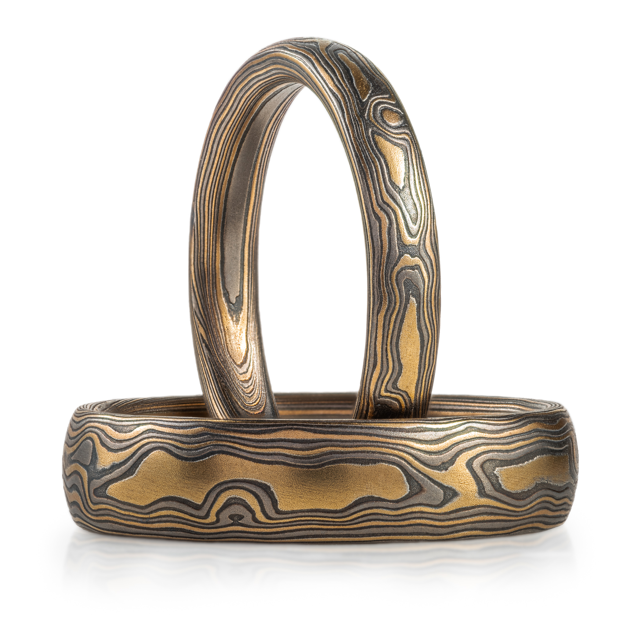 Matching pair of mokume gane rings made to look like woodgrain, made with yellow gold, palladium and silver.