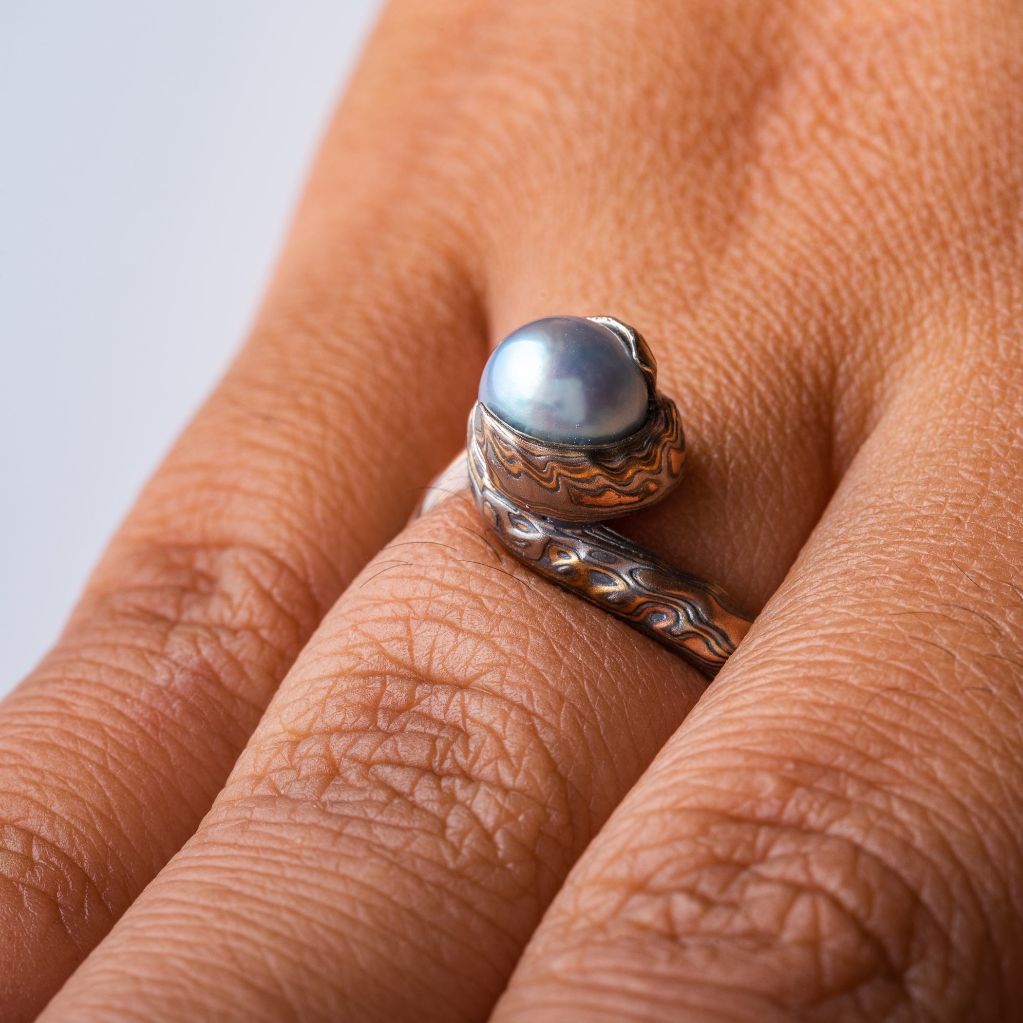 custom blue pearl in a swirled of bypass setting with woodgrain metal all around the pearl holding it in a circle