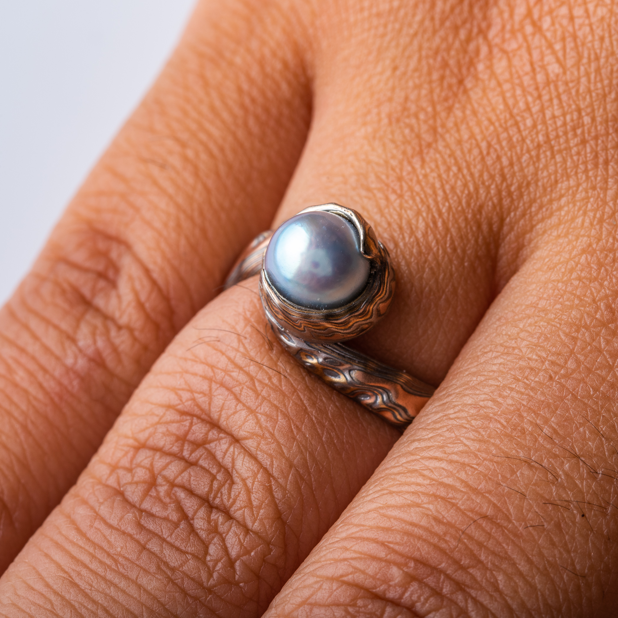 custom blue pearl in a swirled of bypass setting with woodgrain metal all around the pearl holding it in a circle