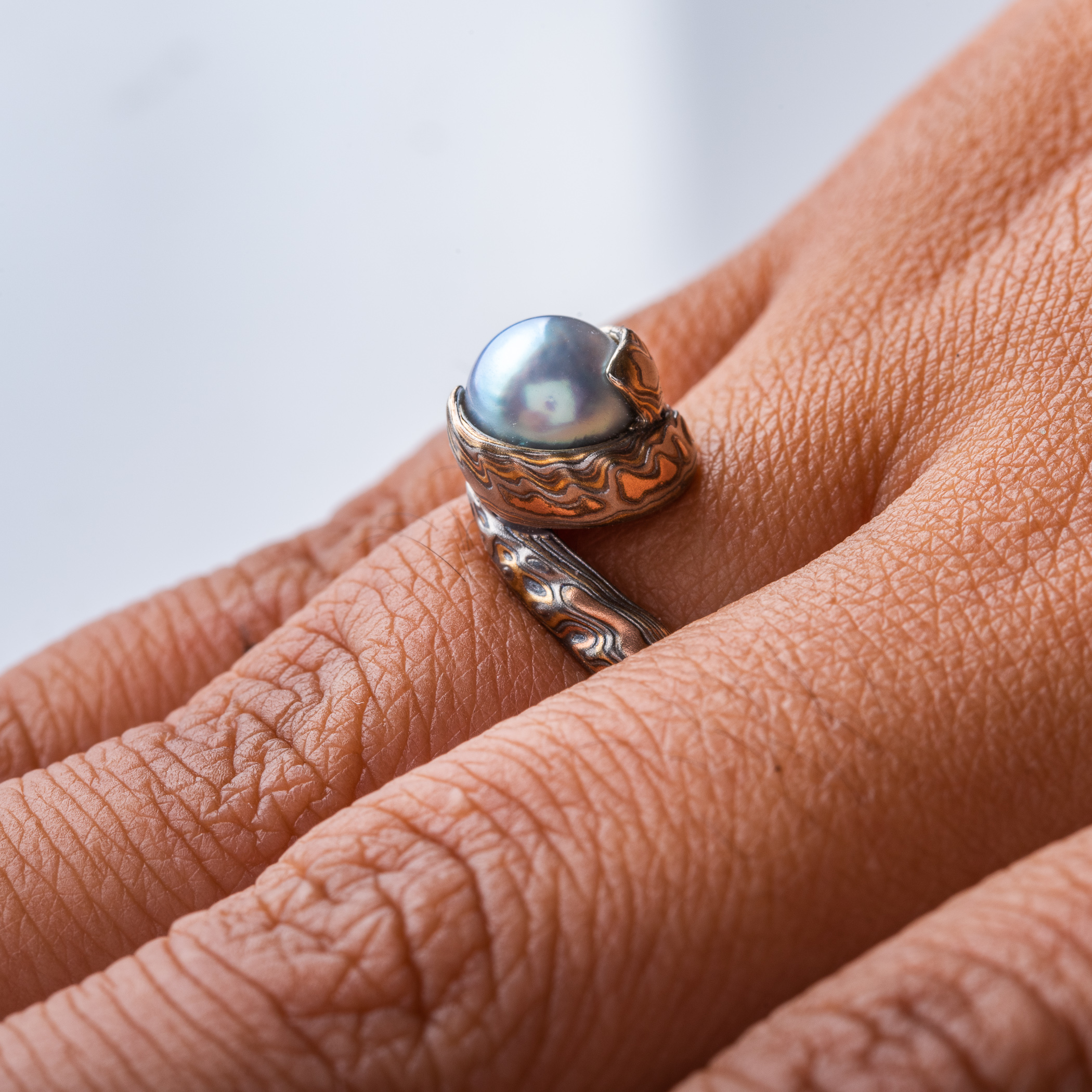 custom blue pearl in a swirled of bypass setting with woodgrain metal all around the pearl holding it in a circle