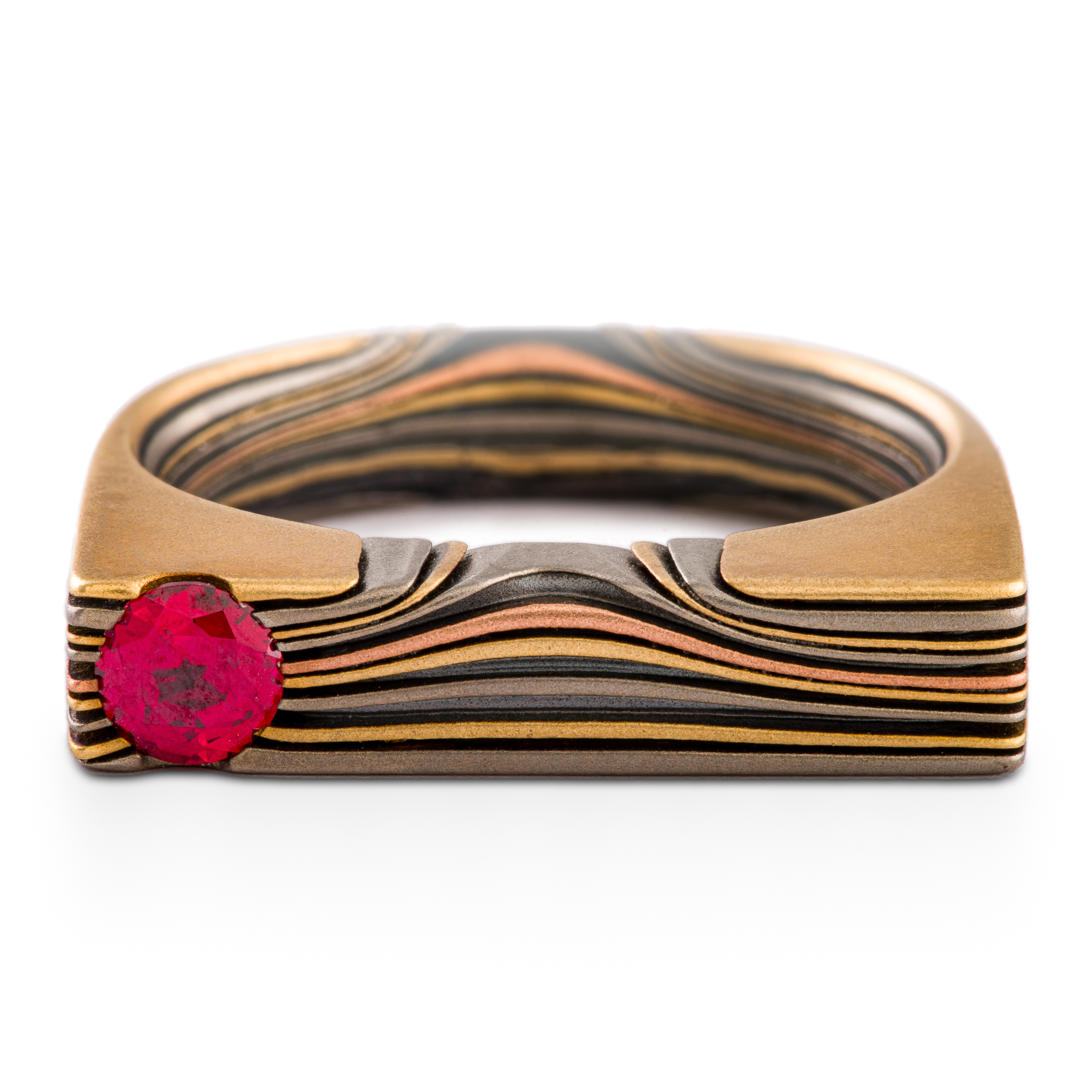 Uniquely shaped flat top mokume gane ring with red stone set flush towards one side. The ring is rounded on the underside for comfort, and made with layers of red and yellow gold, palladium and oxidized silver.