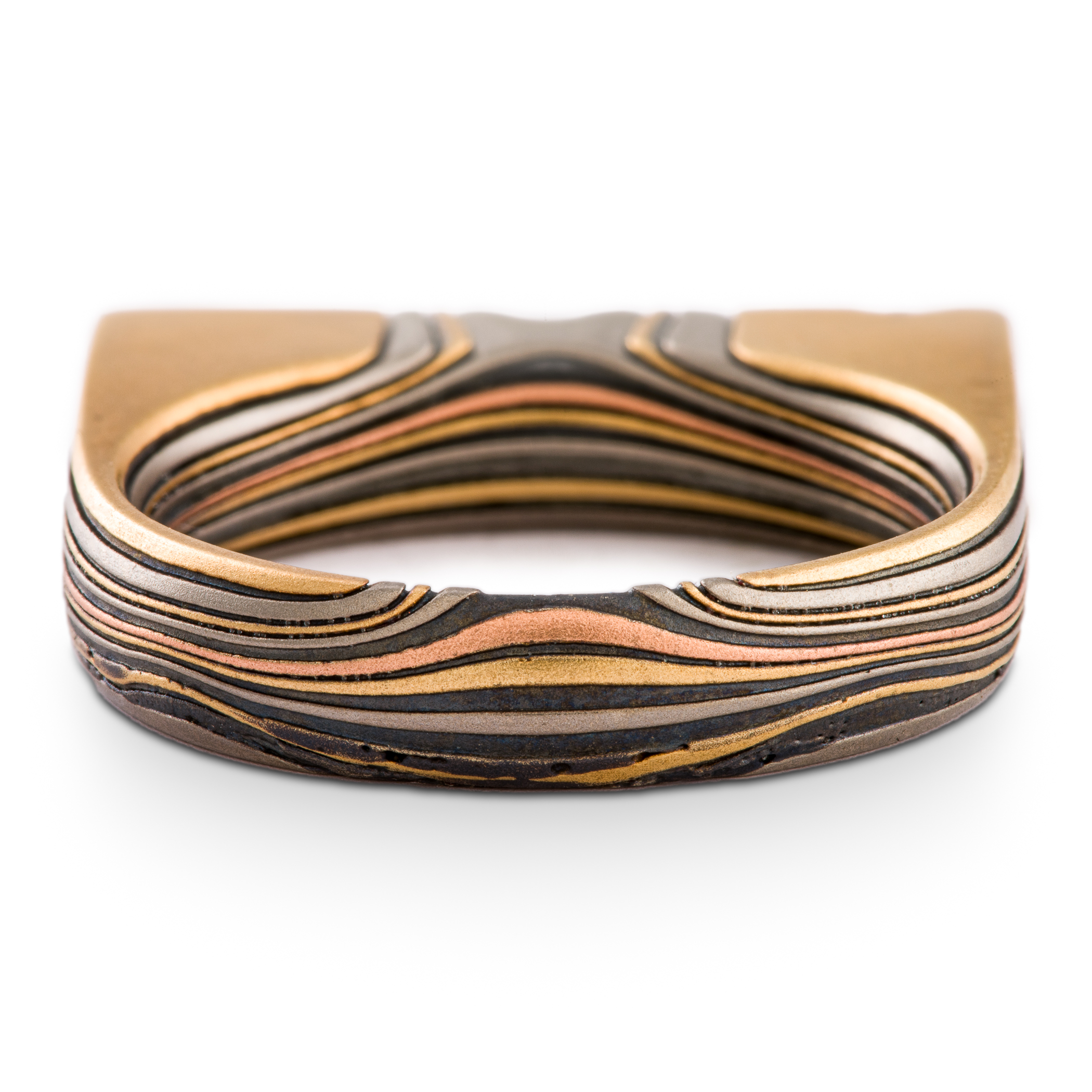 Uniquely shaped flat top mokume gane ring with red stone set flush towards one side. The ring is rounded on the underside for comfort, and made with layers of red and yellow gold, palladium and oxidized silver.