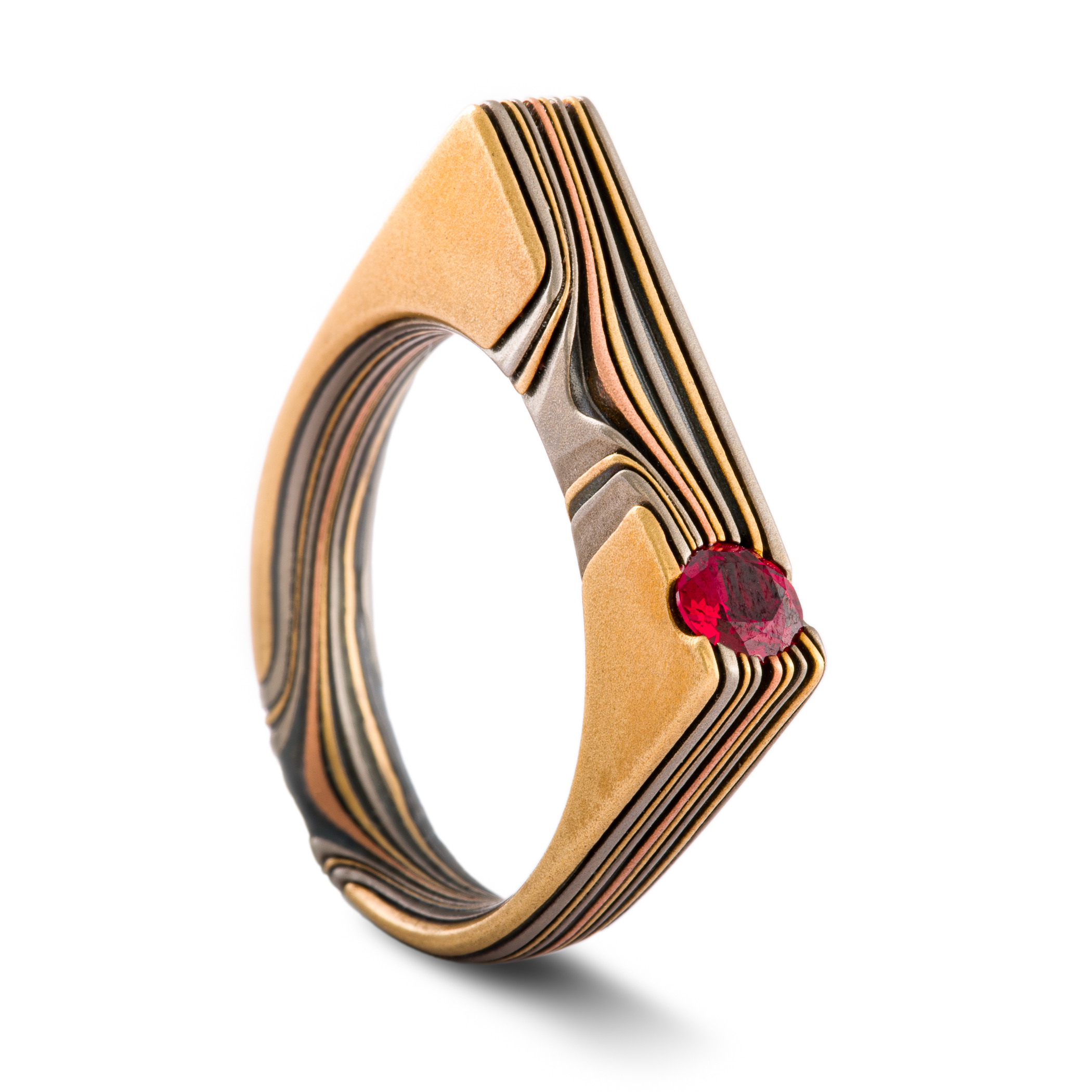 Uniquely shaped flat top mokume gane ring with red stone set flush towards one side. The ring is rounded on the underside for comfort, and made with layers of red and yellow gold, palladium and oxidized silver.