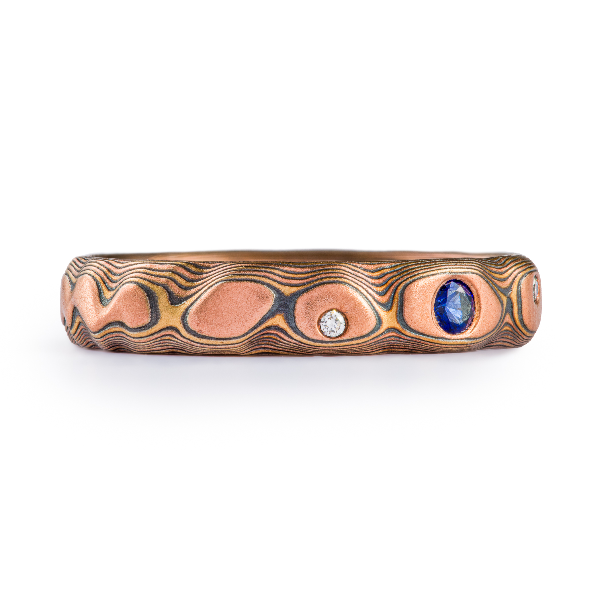 Textured red gold mokume gane ring, with three flush set stones, a slightly larger blue sapphire, flanked by small white stones.
