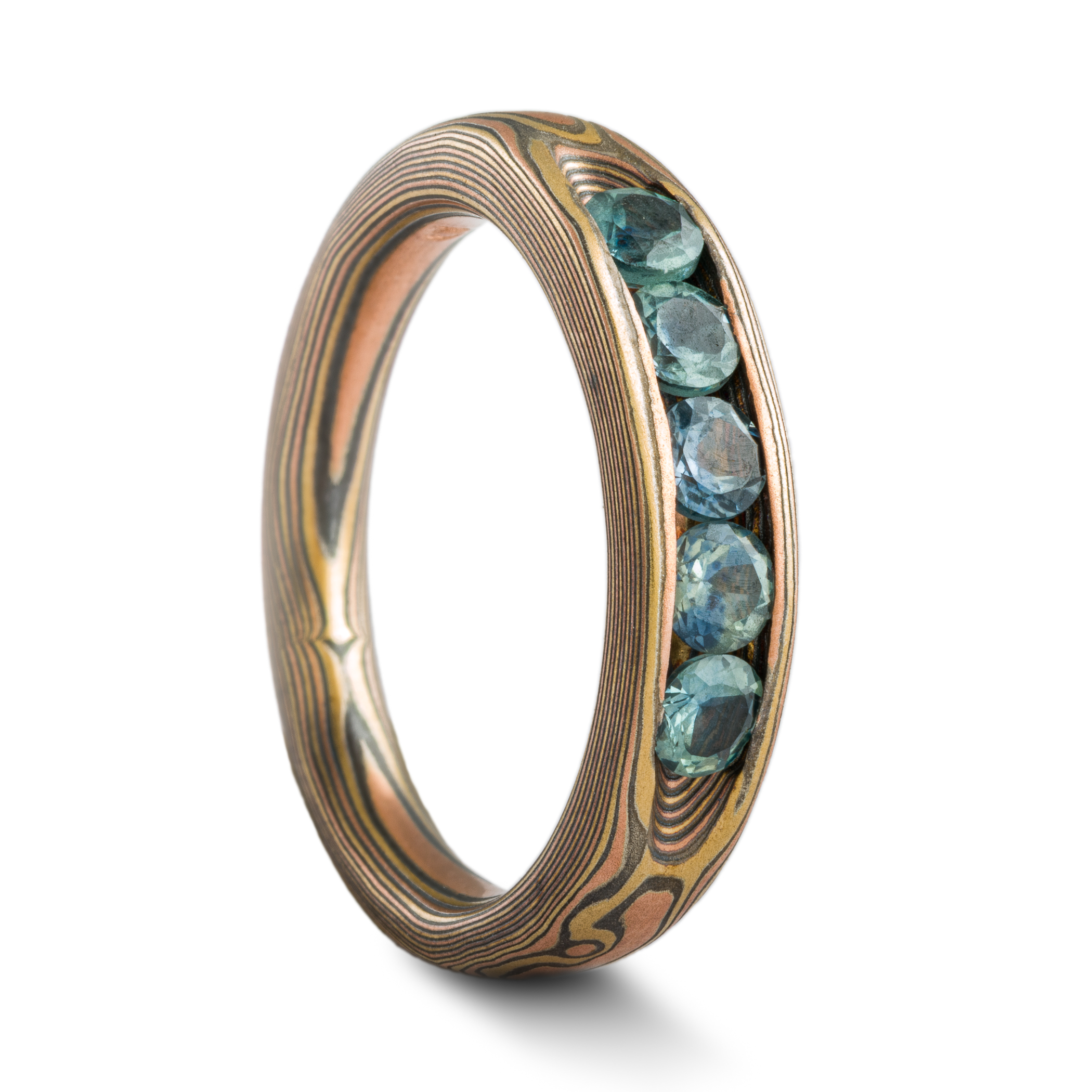 Mokume gane woodgrain patterned ring made with golds and silver, with a line of blue sapphires set into the ring.