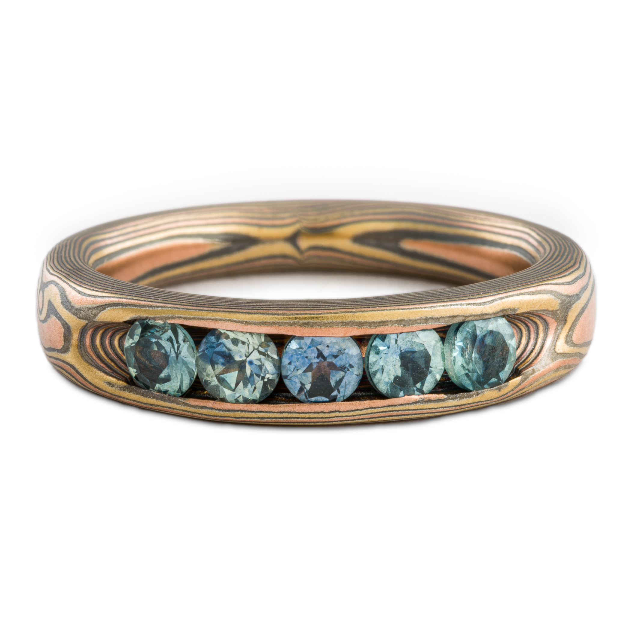 Mokume gane woodgrain patterned ring made with golds and silver, with a line of blue sapphires set into the ring.
