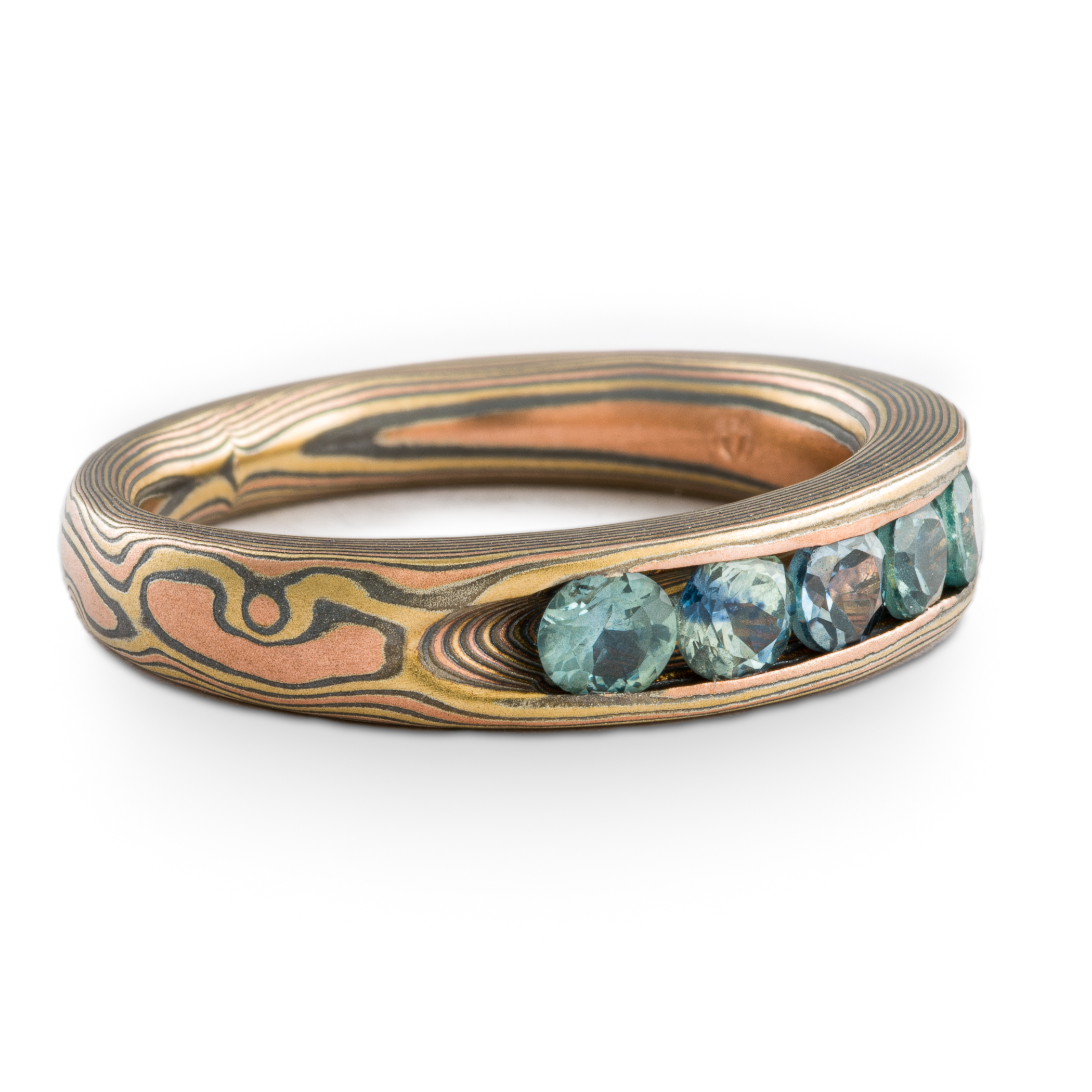 Mokume gane woodgrain patterned ring made with golds and silver, with a line of blue sapphires set into the ring.