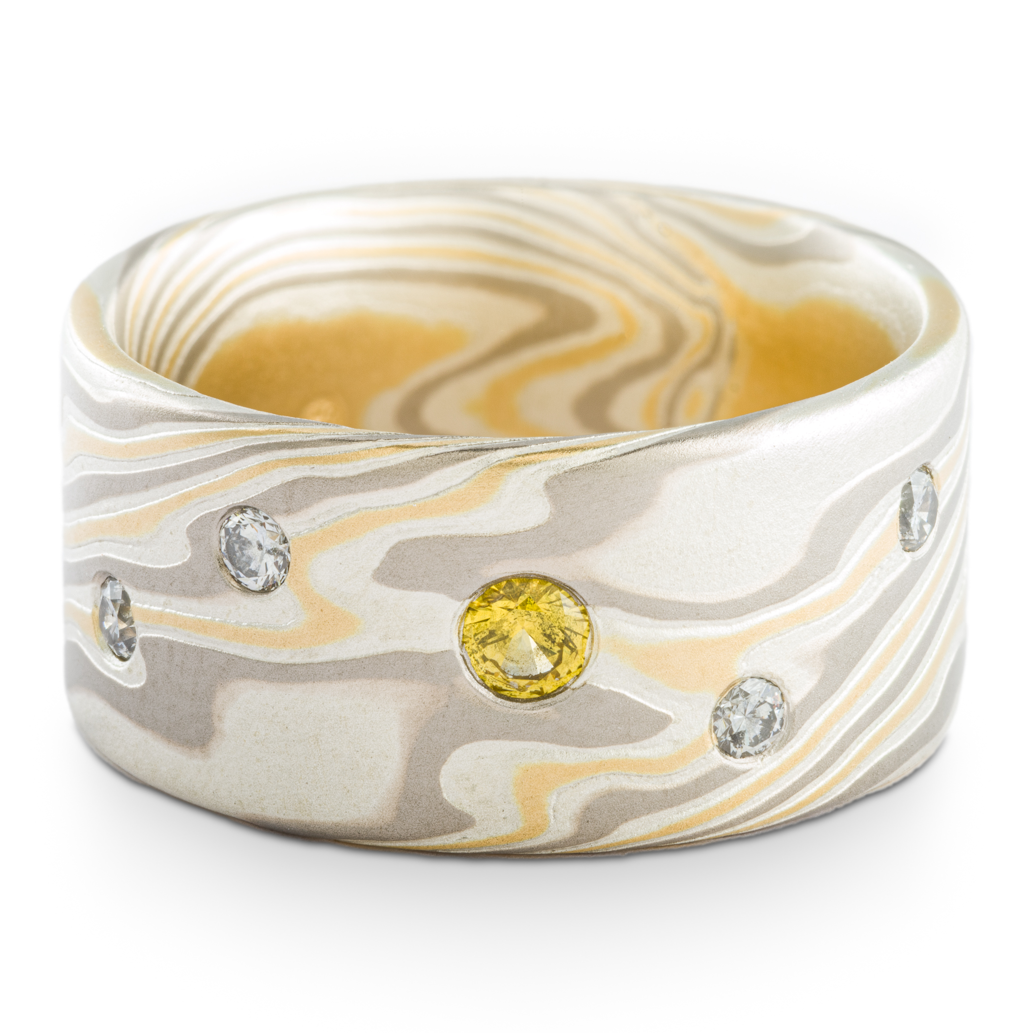 Mokume gane patterned ring made with yellow gold, palladium and silver, with small round yellow and white stones set into the wide, flat profile band.