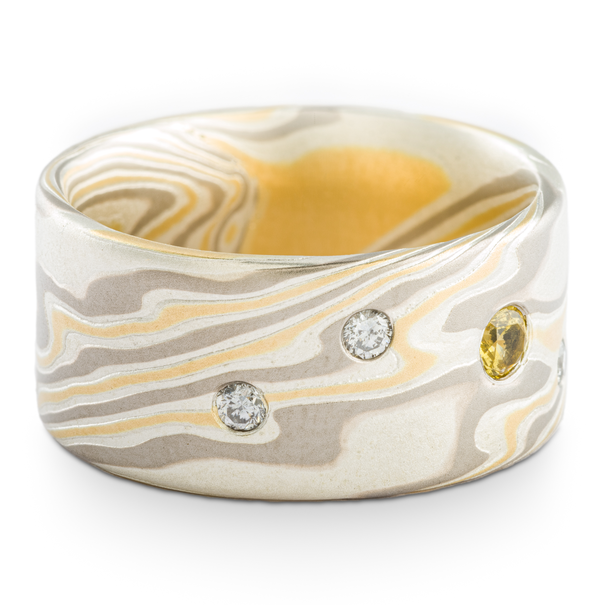 Mokume gane patterned ring made with yellow gold, palladium and silver, with small round yellow and white stones set into the wide, flat profile band.