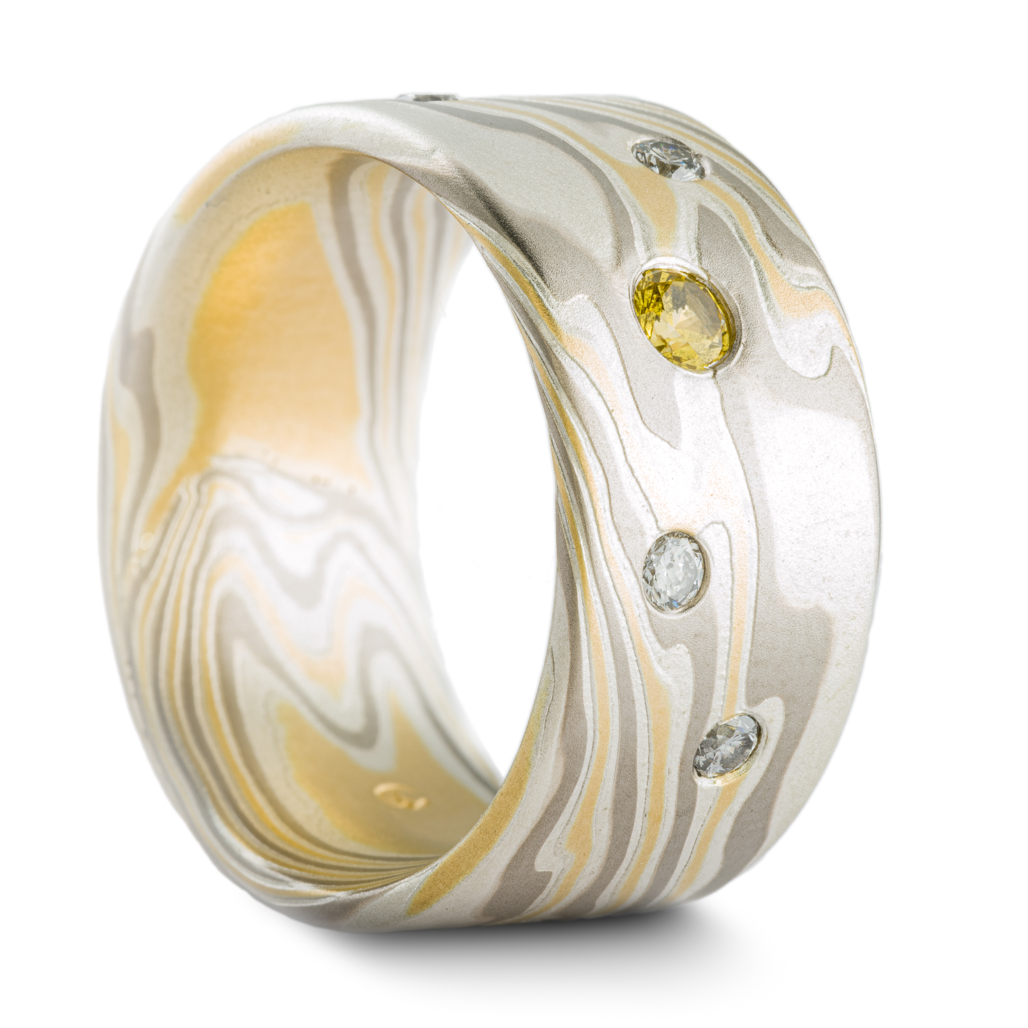 Mokume gane patterned ring made with yellow gold, palladium and silver, with small round yellow and white stones set into the wide, flat profile band.