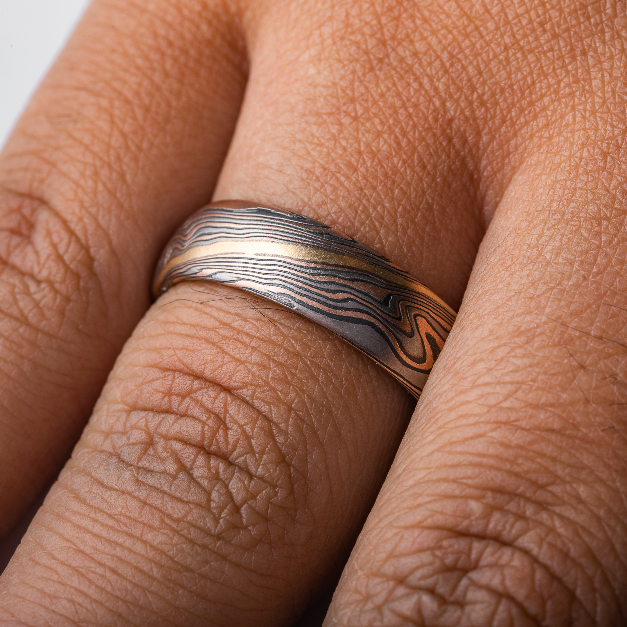hand carved and handmade twisted metal and stripes of gold. yellow gold , red gold, silver and palladium swirled metal. wide, carved ring for a man