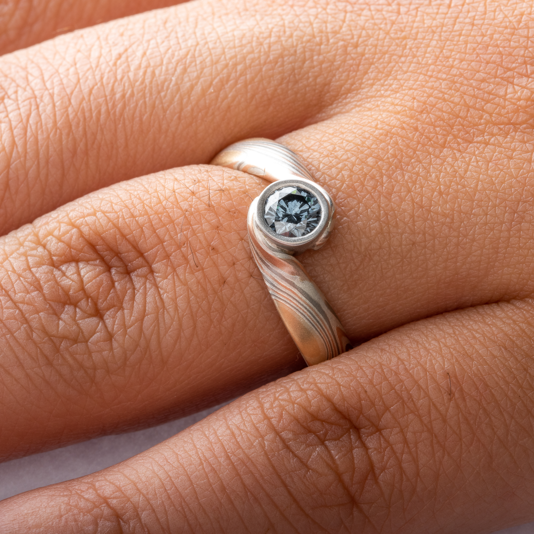 Blue Diamond mokume gane ring made with golds, palladium and silver in a swirling pattern, with a gently sloping and twisted band.