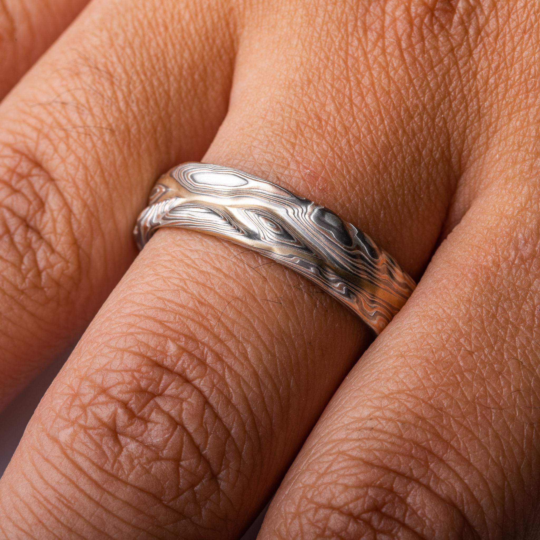 hand carved and handmade twisted metal and stripes of gold. iyellow gold , red gold, silver and palladium swirled metal. wide, carved ring for a man