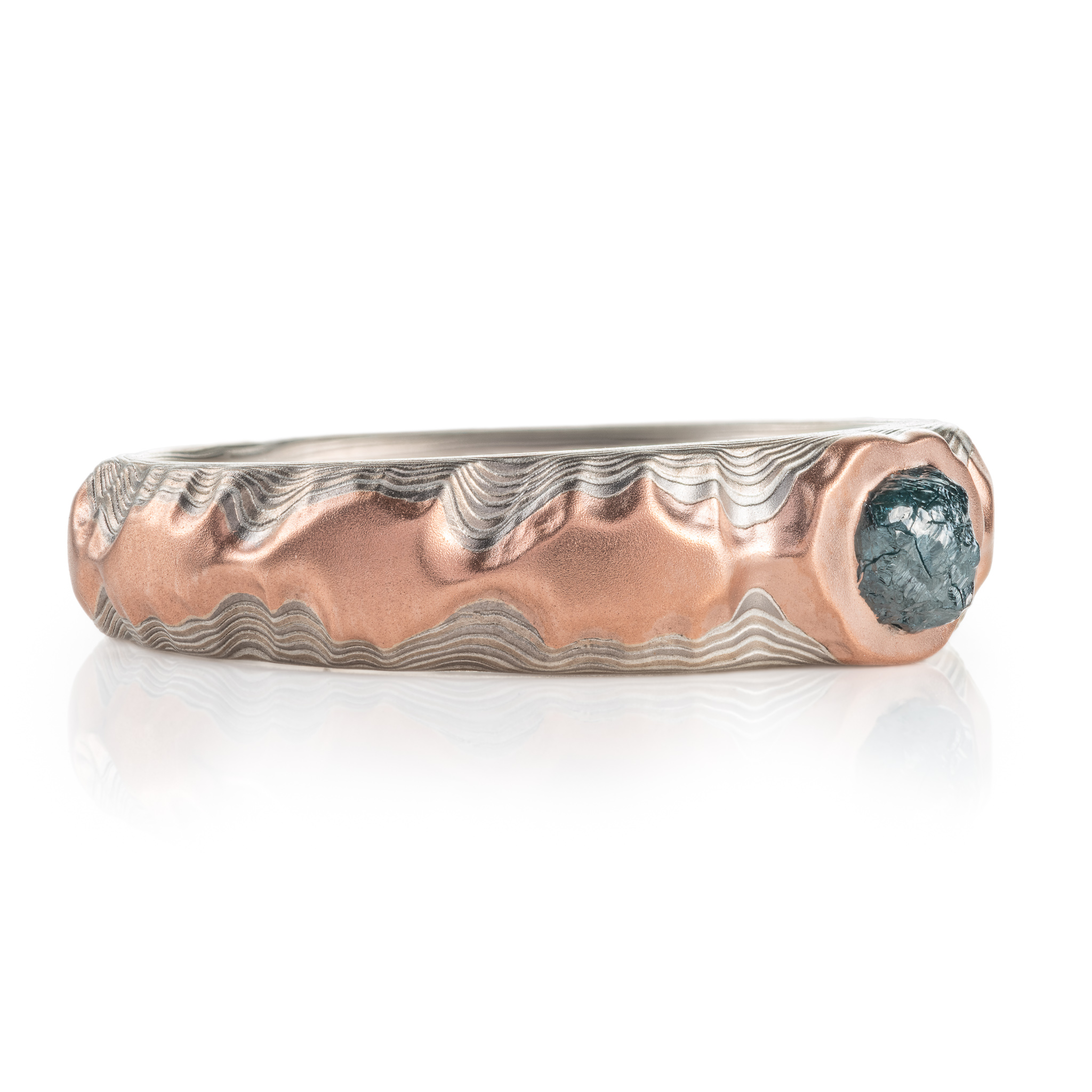 guri bori patterned ring with a ridgeline style, mountains of red gold running around the ring, with a larger mass of red gold holding a blue diamond crystal