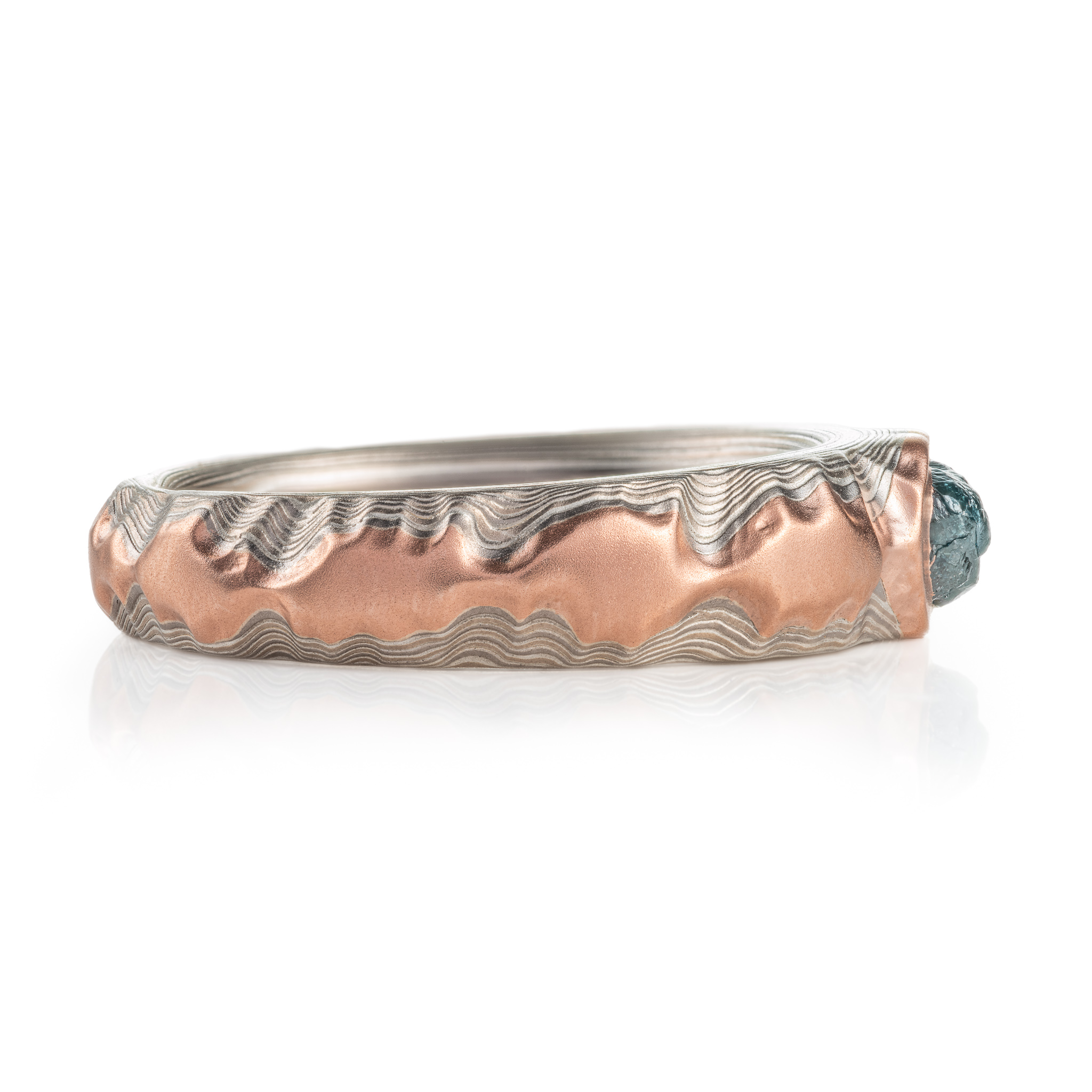 guri bori patterned ring with a ridgeline style, mountains of red gold running around the ring, with a larger mass of red gold holding a blue diamond crystal