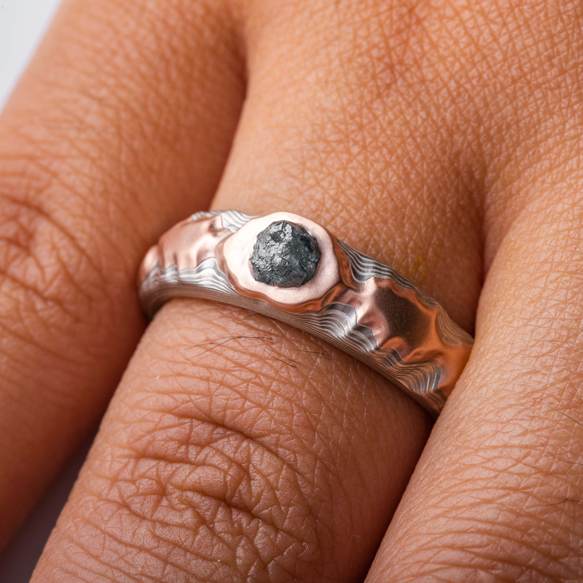 guri bori patterned ring with a ridgeline style, mountains of red gold running around the ring, with a larger mass of red gold holding a blue diamond crystal