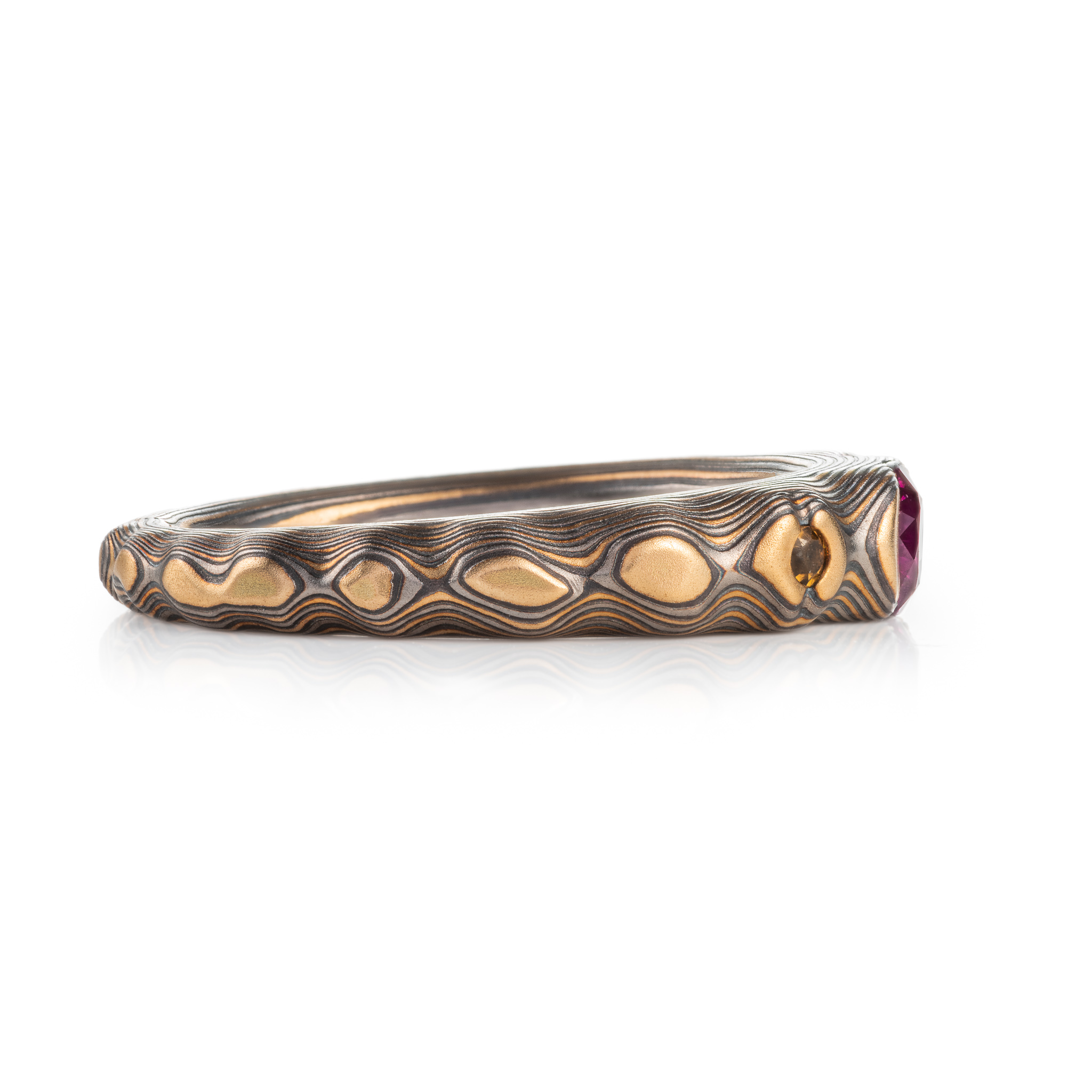 pink purple sapphire with cognac diamonds set in a mokume band of yellow gold, silver and palladium. the stones are set in yellow gold islands