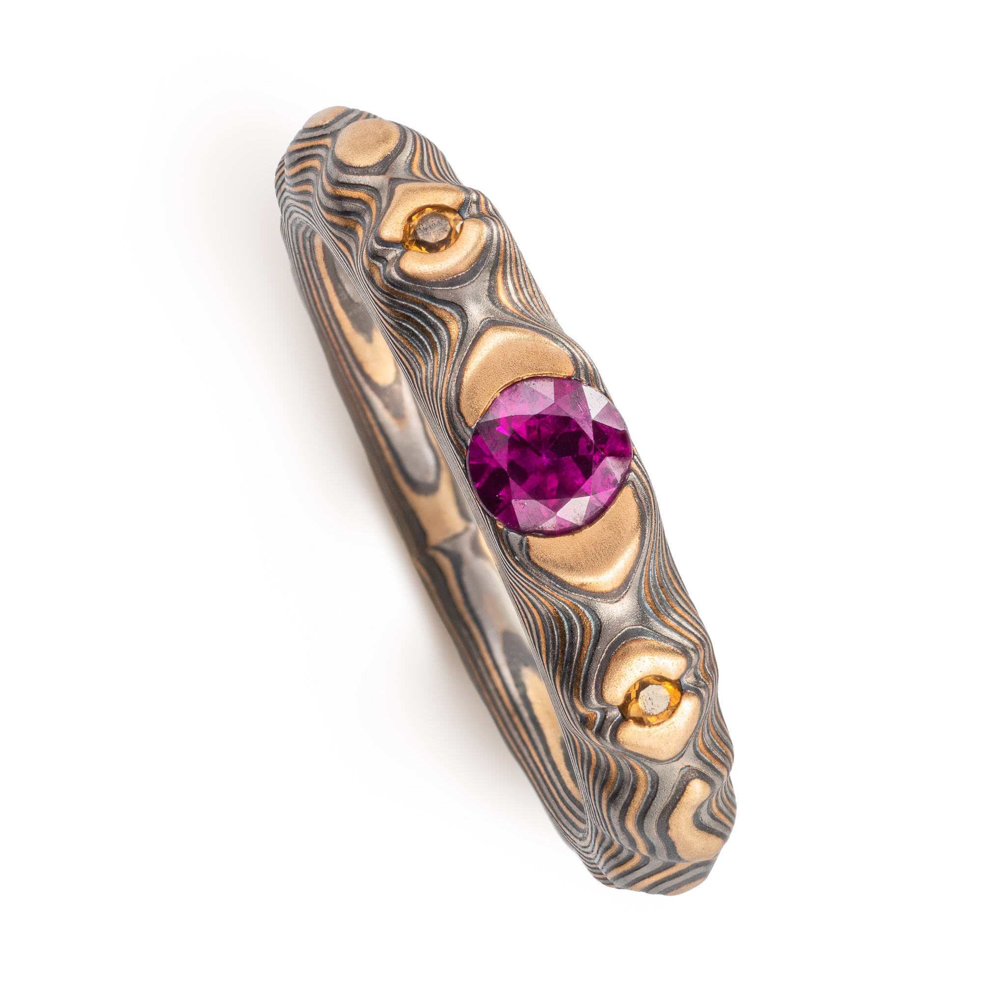 pink purple sapphire with cognac diamonds set in a mokume band of yellow gold, silver and palladium. the stones are set in yellow gold islands