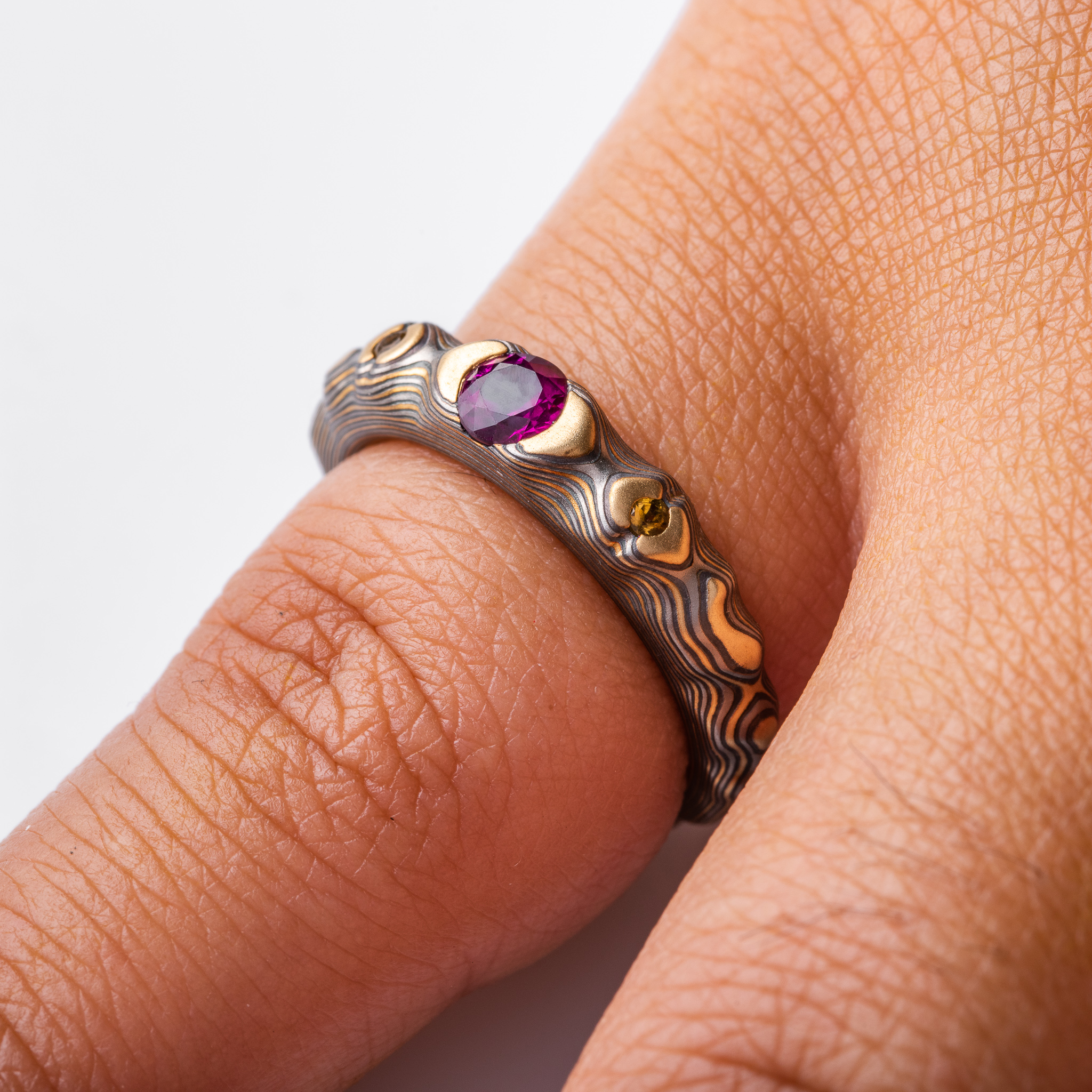 pink purple sapphire with cognac diamonds set in a mokume band of yellow gold, silver and palladium. the stones are set in yellow gold islands